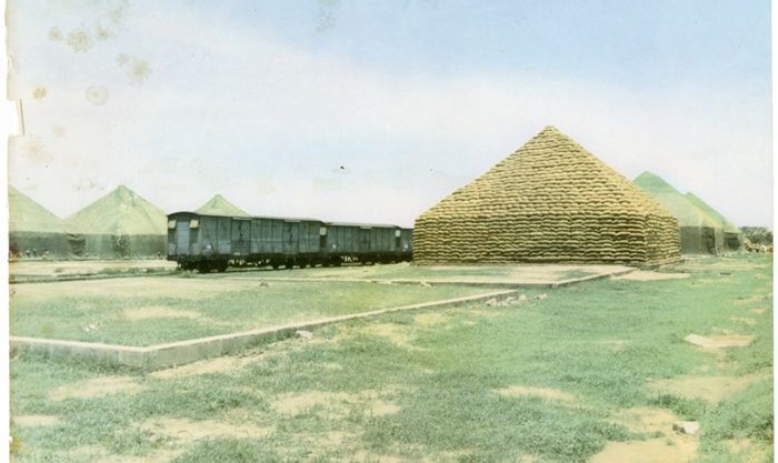 Reproduction of a colour photograph of pyramids of groundnuts with a locomotive taken by the Nigerian Railway Public Relations Division, Ebute-Metta, Lagos. (The rail system helped transport commodities such as groundnuts produced from Northern Nigeria to the port of Lagos).