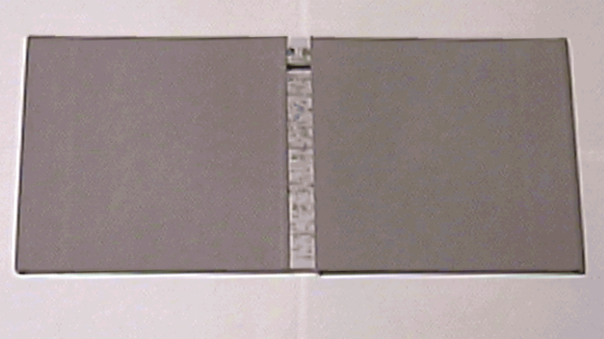 A grainy image of a book taken from a VHS recorder on a white background. The book is across the image and is a medium gray color. There are two covers meeting in the middle with space between them.