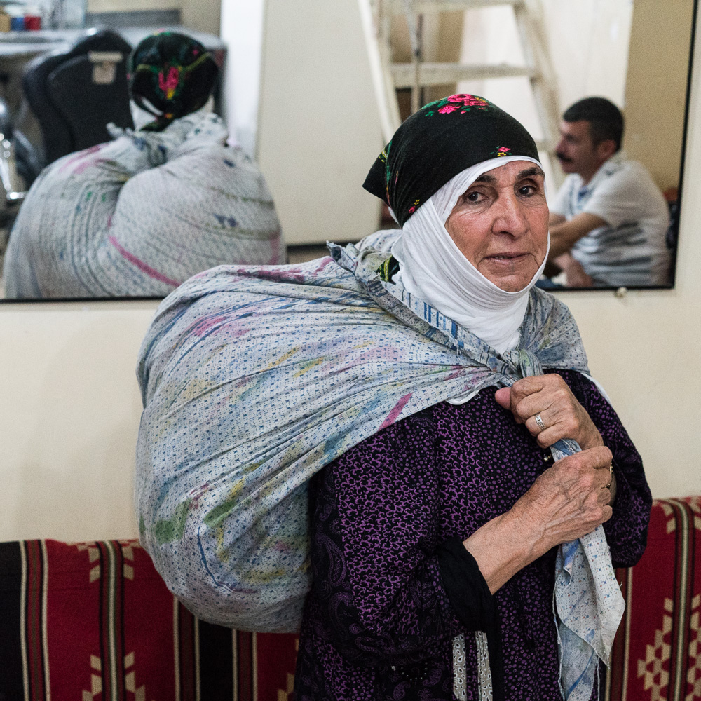 N&eacute;e &agrave; Nusaybin, Cemile habite depuis 55 ans dans le quartier de Sur o&ugrave; elle et son mari avaient d&eacute;cid&eacute; de vivre car il &eacute;tait plus facile d'y trouver du travail &agrave; l'&eacute;poque. A pr&egrave;s de 76 ans - voire plus, glisse un de ses fils - son regard est toujours vif et p&eacute;tillant, elle d&eacute;borde d'&eacute;nergie. Avant les combats, elle poss&eacute;dait une grande maison, avec un jardin et des arbres fruitiers, o&ugrave; un de ses fils avaient &eacute;galement une boutique de tailleur. Elle, faisait du porte &agrave; porte pour vendre des v&ecirc;tements et de la lingerie ramen&eacute;s de Syrie."Un jour les jeunes sont venus nous voir, ils nous ont dit qu'ils construisaient les barricades". Puis &ccedil;a a &eacute;t&eacute; le couvre feu, la fuite en abandonnant toute sa vie derri&egrave;re elle, la maison dans laquelle elle pensait mourir en paix un jour. Aujourd'hui elle vit dans un autre quartier de Sur avec sa famille, mais elle est de nouveau menac&eacute;e d'expulsion par l'&eacute;tat qui veut raser certaines zones dans le cadre du projet de reconstruction de Sur.Aujourd'hui, elle parcourt de nouveau les rues et les villages, son baluchon de v&ecirc;tements sur l'&eacute;paule, pour gagner de quoi se nourrir. "Est-ce que j'ai le choix ?