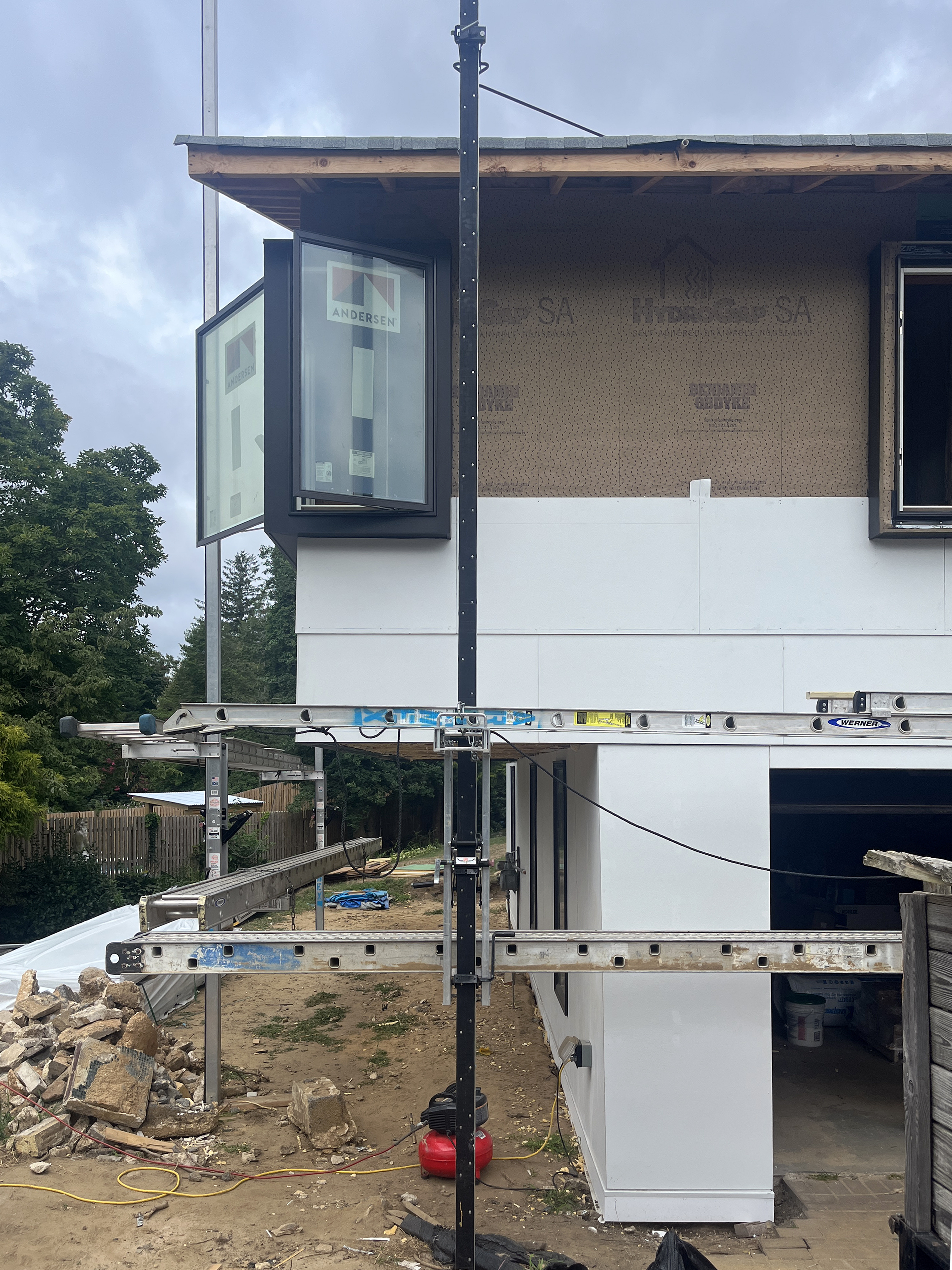 Construction progress photograph of the Atlantic Highlands Ranch Reno, showing the left side wall with white cladding installed beneath the second-story eaves and a prominent casement window.