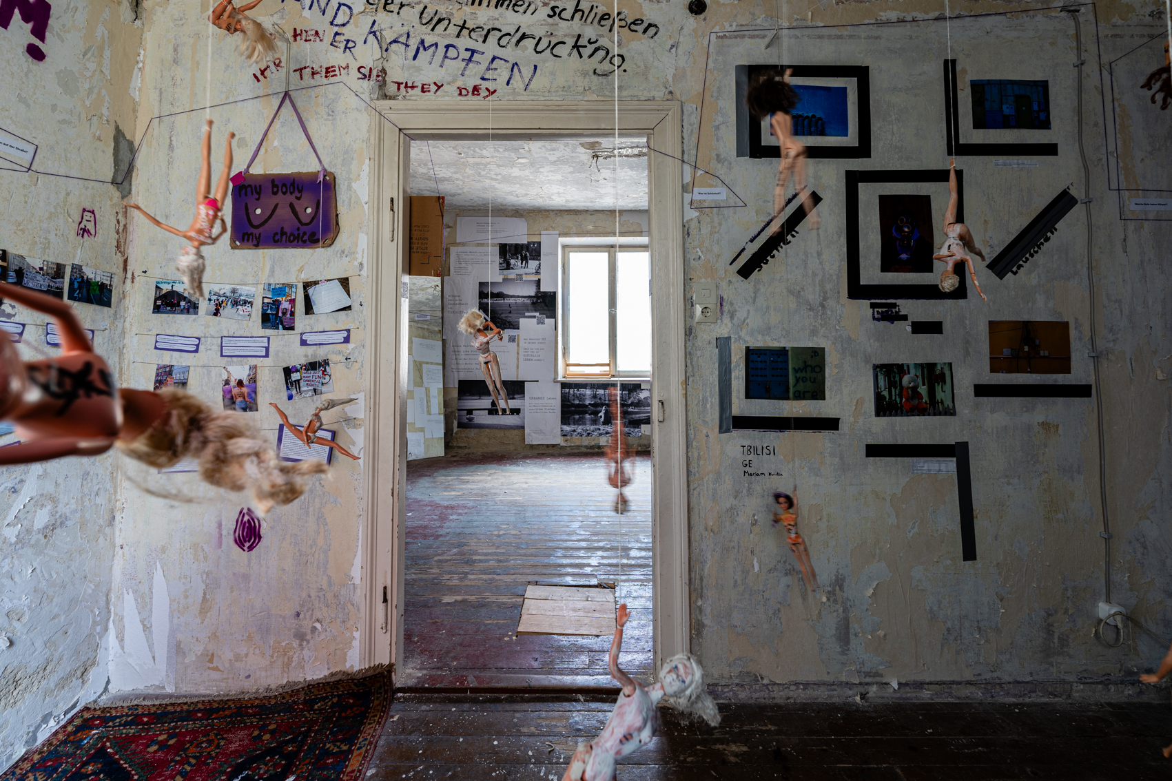 Bild 2 zu Patriarchat abnippeln: Im Raum stehend auf die Eingangst&uuml;r des Raumes schauend. An der Wand rechts der T&uuml;r sind Fotografien von Ausschnitten aus Tbilisi  zu sehen.