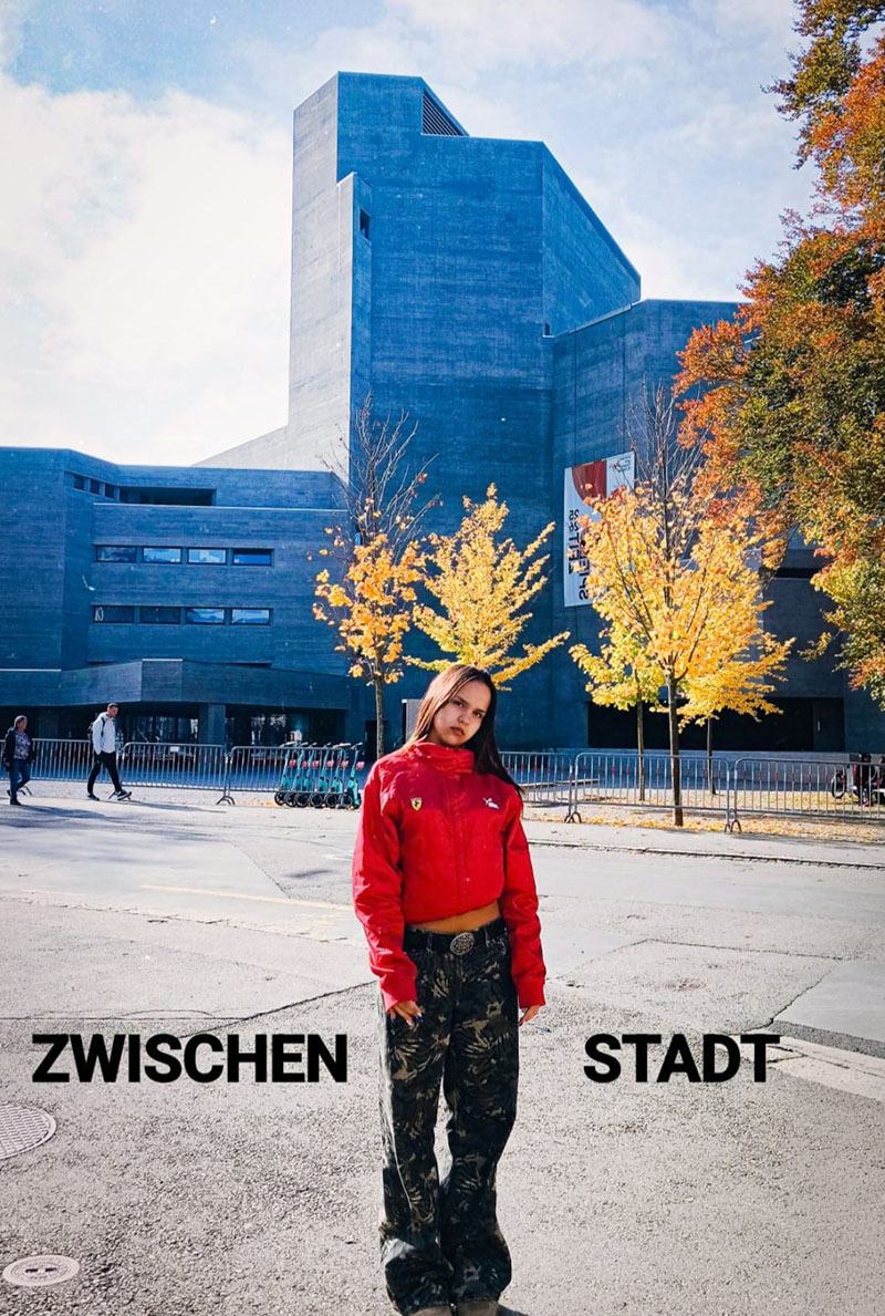 Hinter Eli laufen zwei Menschen vor einem leeren Theater. F&uuml;nf Meter vor ihr sind Zehntausende gerade auf dem Jahrmarkt.