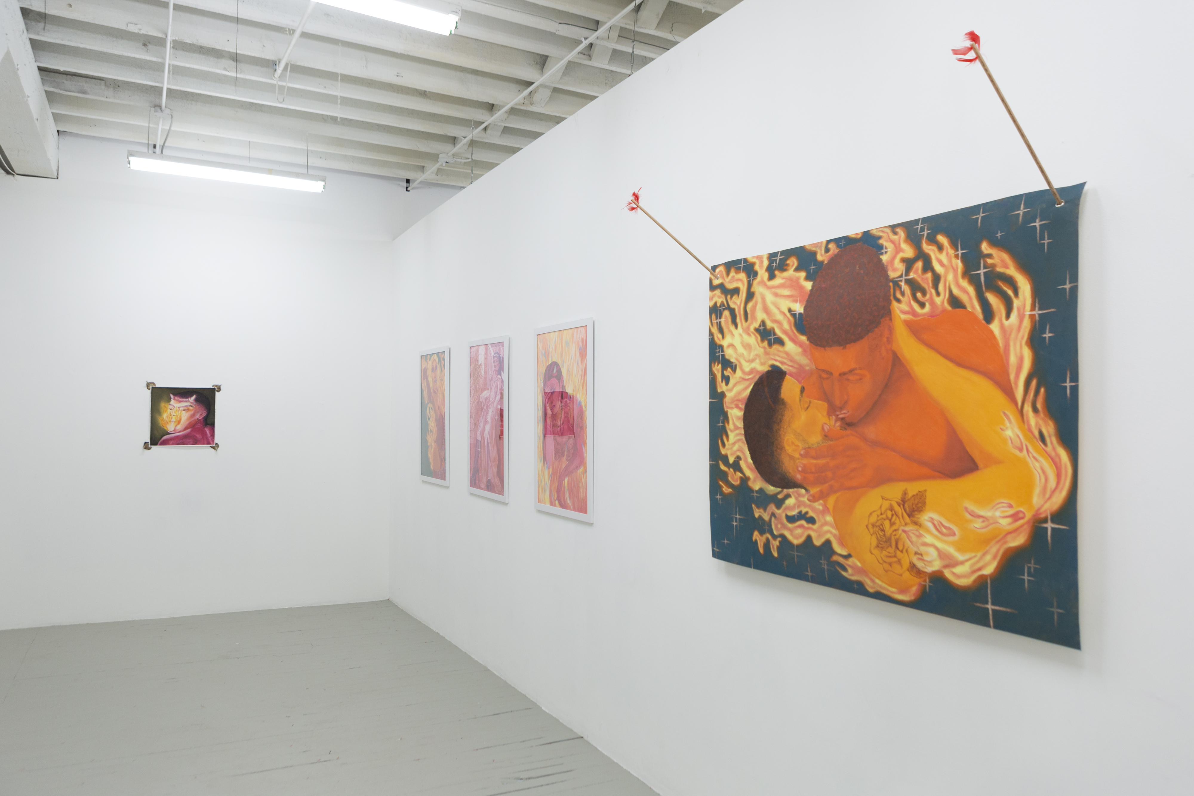 Installation image from the exhibition Amor de mis Amores. In focus is a drawing of two orange male figures surrounded by fire on a blue background. The drawing is held into the wall by two arrows.