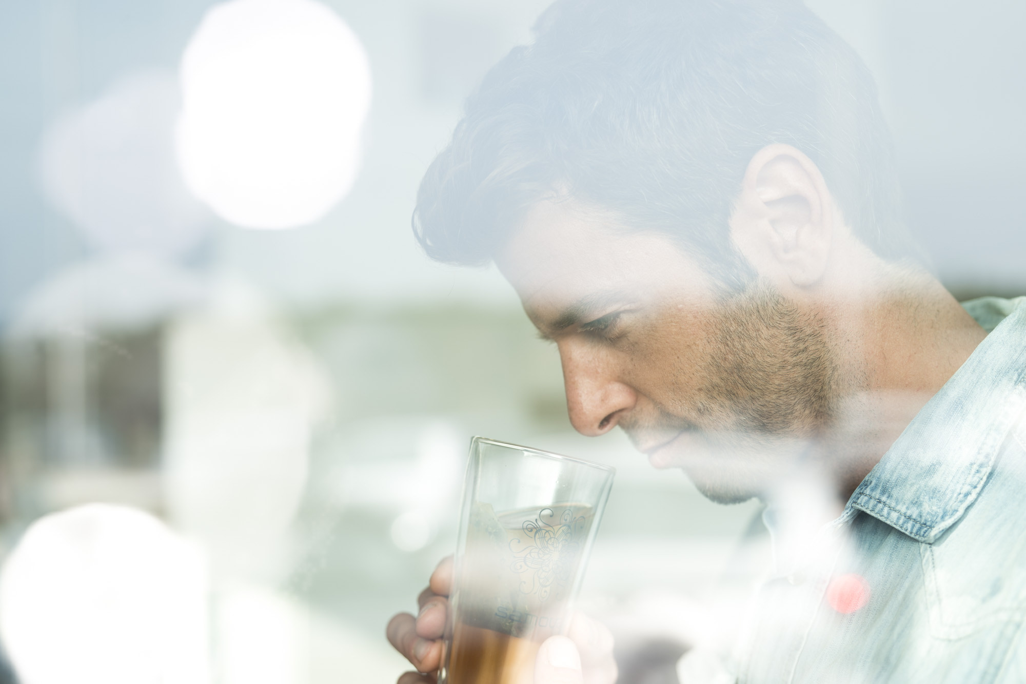 Portrait eines jungen Mannes mit einem Teebecher in der Hand. Portrait durch eine Scheibe mit Bendenflecken.