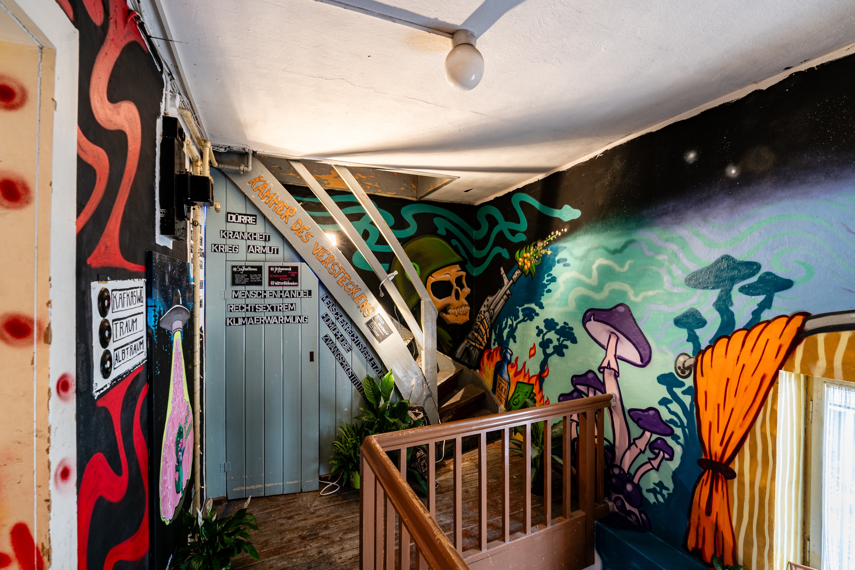 Bild 2 zu Beyond wildest Dreams:  Weitere Bemalungen der W&auml;nde vom Gang des obersten Stockwerkes zeigen eine Art Traumwelt. Pilze, Totenk&ouml;pfe und Schlangenformen sind erkennbar. Rechts ist ein Treppengel&auml;nder, das in den Dachboden f&uuml;hrt. Darunter befindet sich das Kunstwerk "Kammer des Versteckens".