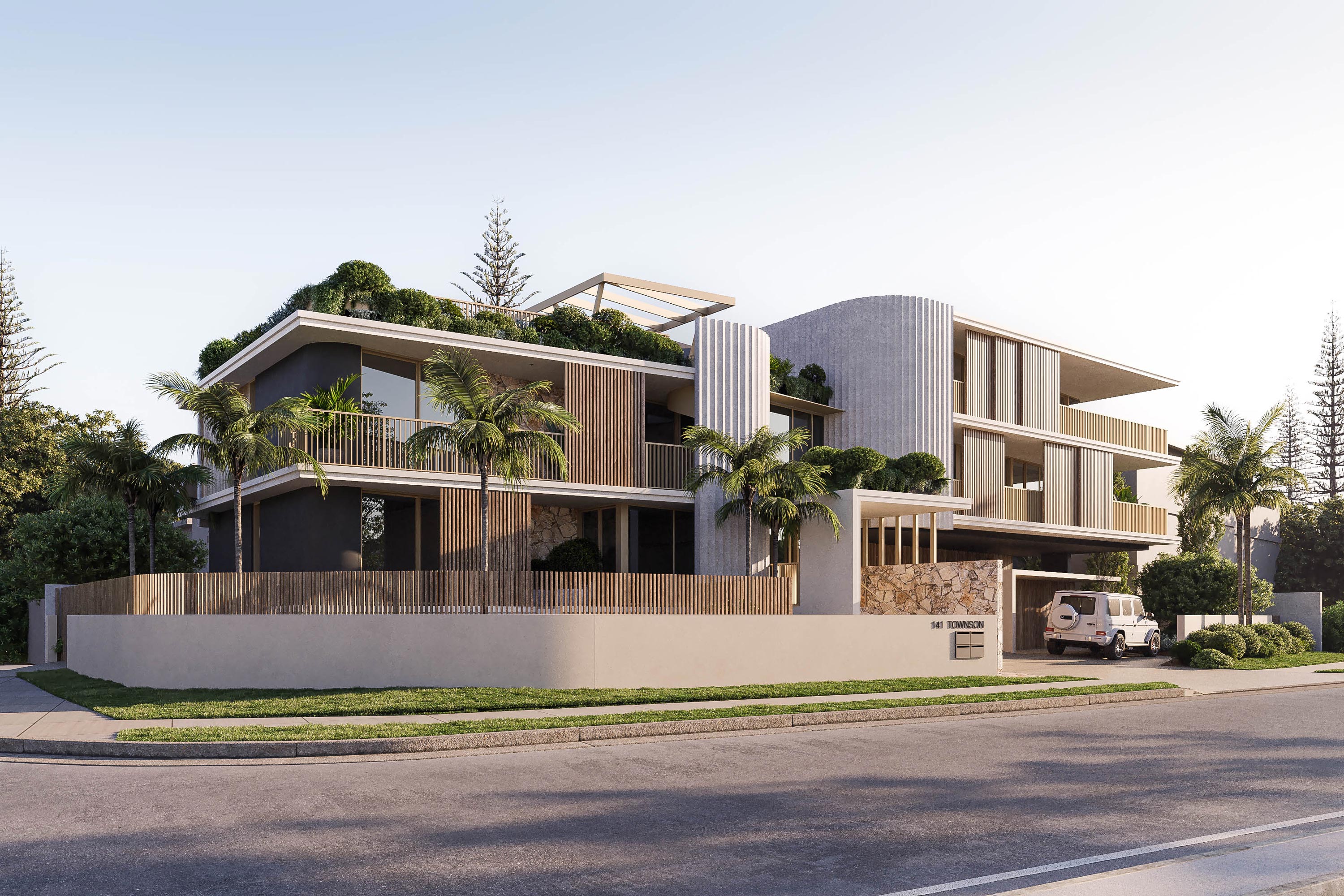 Modern multi-level luxury apartment building with off-white concrete, vertical timber battens, stone accents, and large balconies with timber railings. Green rooftop garden, surrounded by palm trees and tropical landscaping. White SUV parked at the gated entry marked "141 Townson." Sunny day with clear skies.