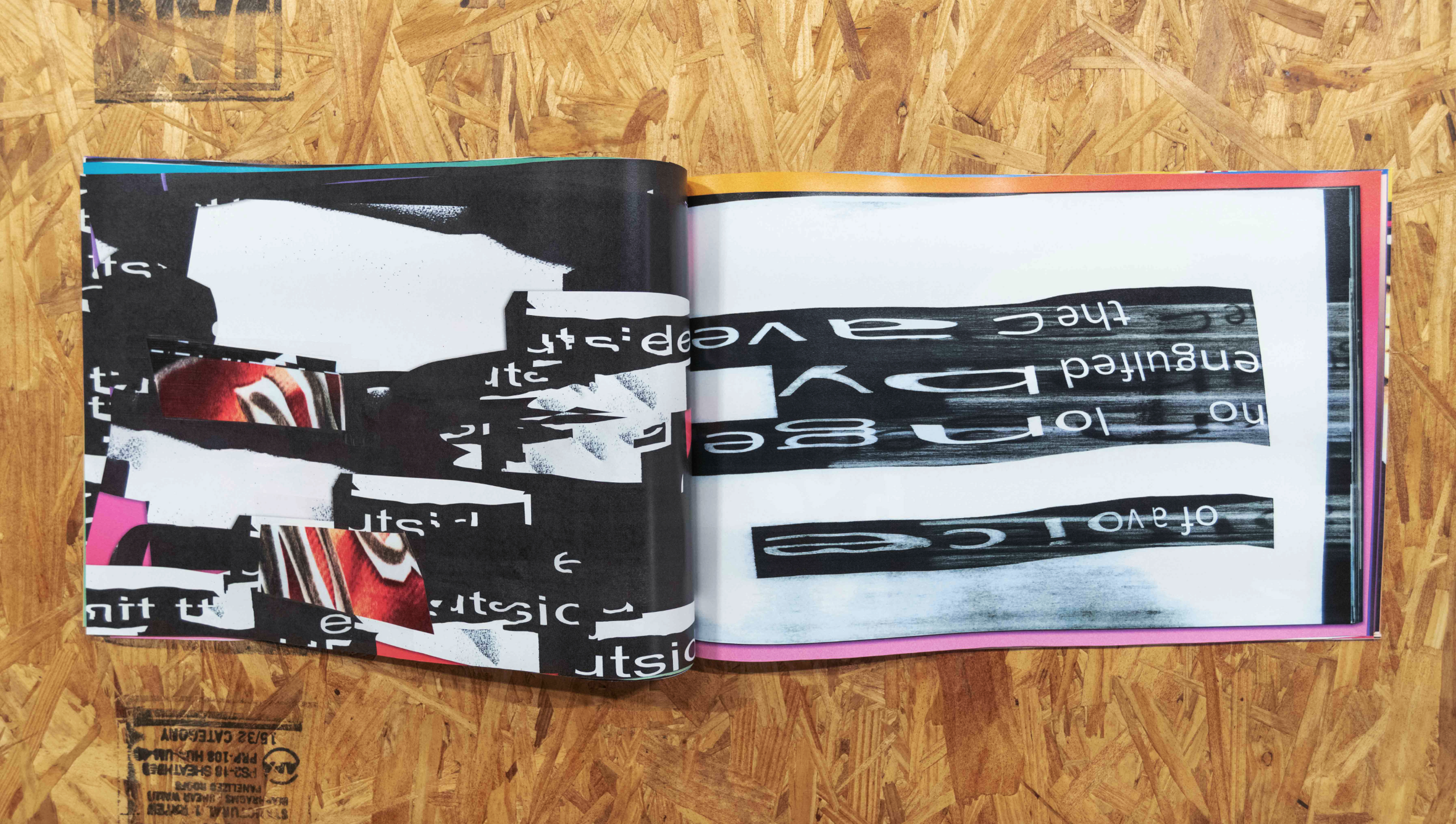 An artist book is open on a wooden table top. It shows a xerox-collage of warped letters and tetures, in black, white, and orange tones.