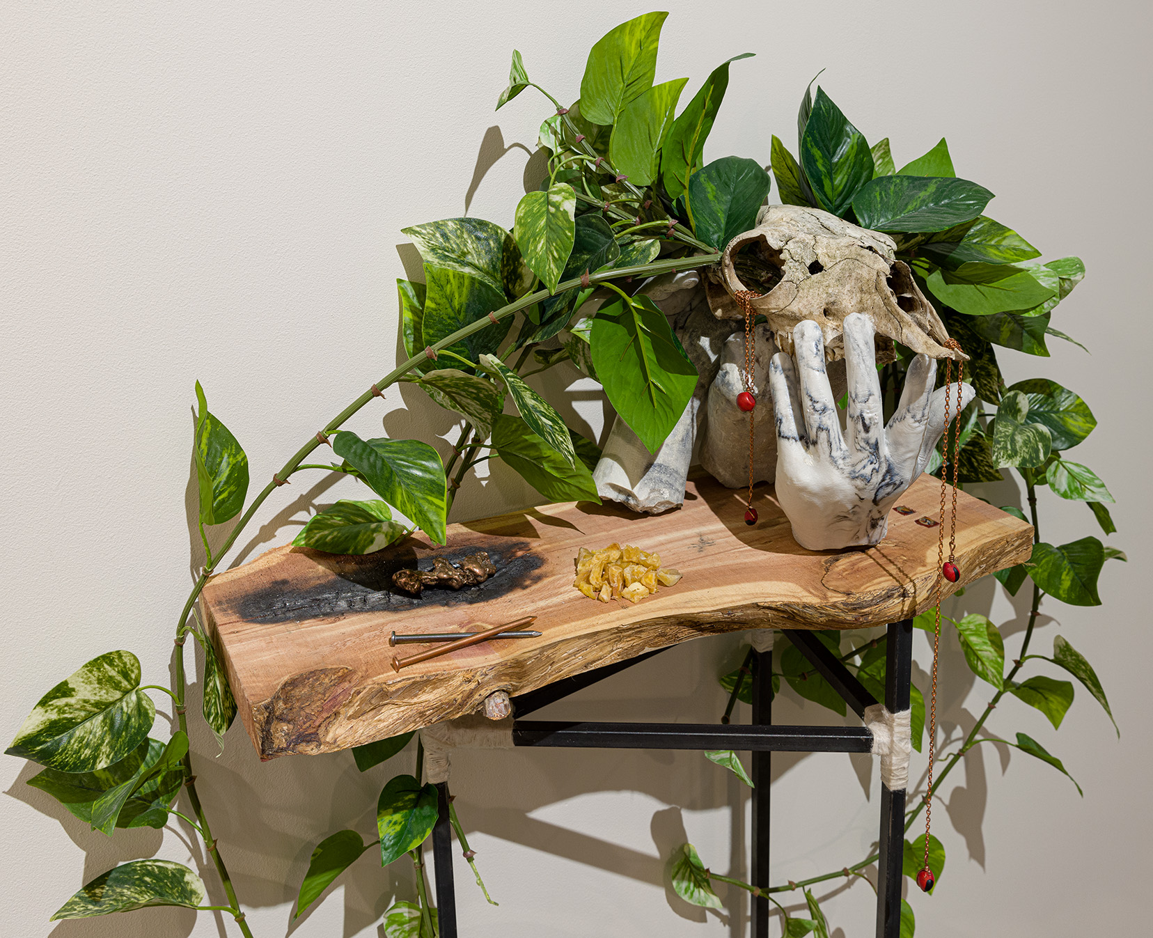 Dante Migone-Ojeda, "Amaru," 2023, red cedar, copper, steel, cast stone, alpaca skull, alpaca wool, artificial pothos, Huayruro seeds, medallion, prayer beads, dried yellow potatoes, wax, slag, 54 x 30 x 12 inches. Photo by Etienne Frossard. 