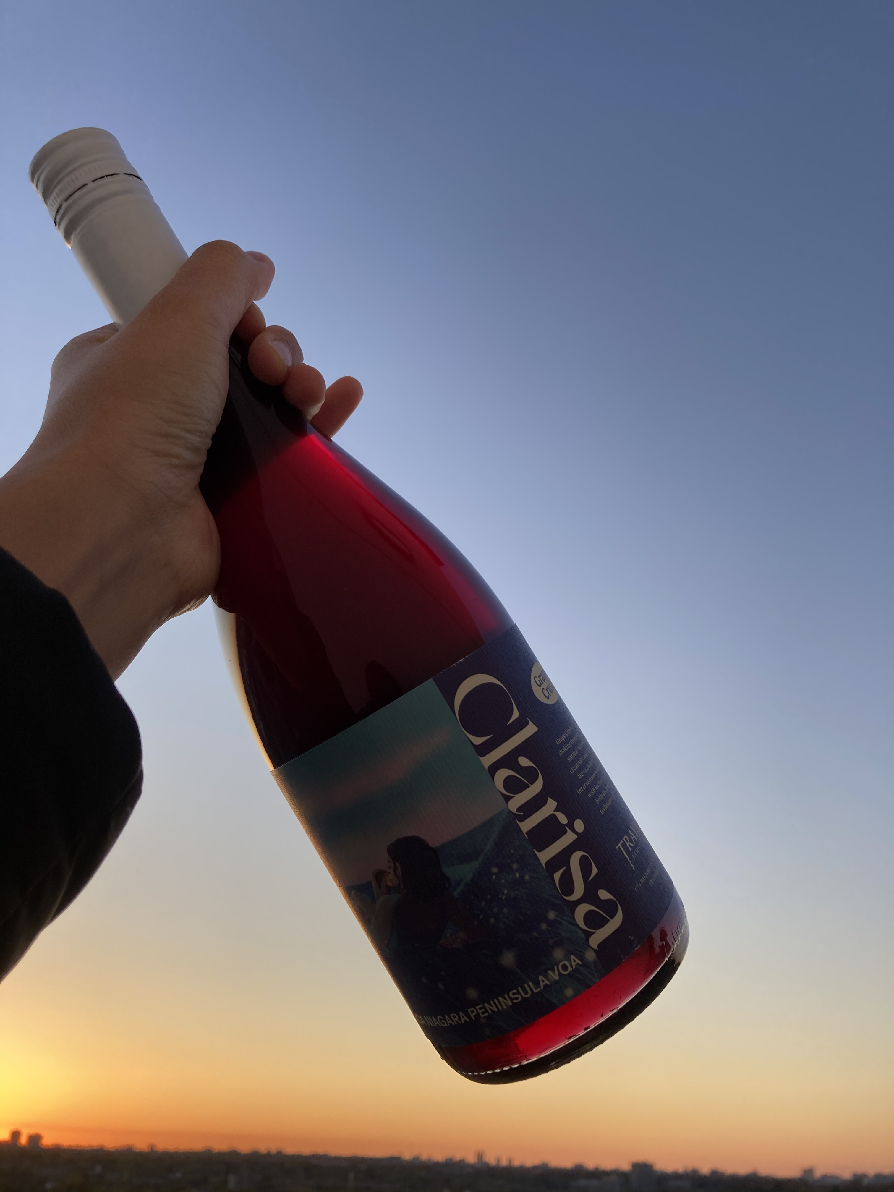 A photo of the Clarisa illustration on a wine bottle. The wine is a deep red, and illuminated from behind by the sunset.