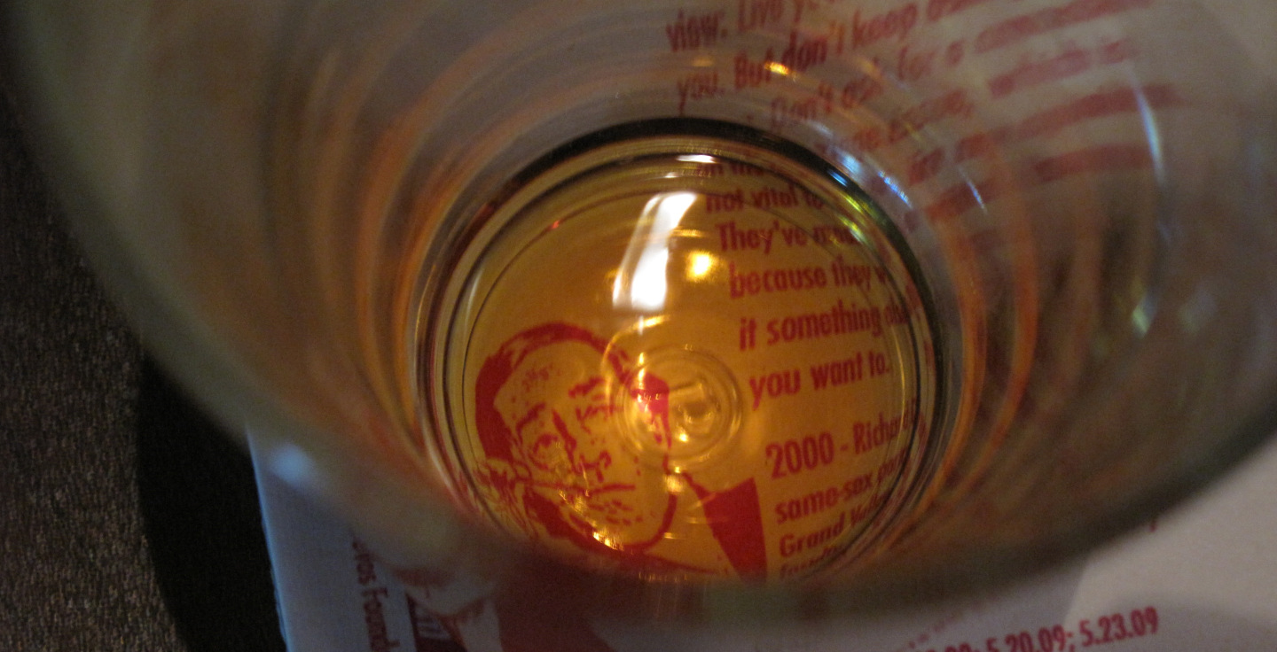 a pink rendering of Richard Devos printed on a coaster; image shot from overhead through an empty beer glass
