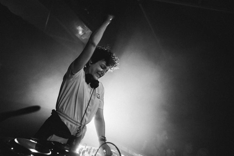 Annie Mac raising her hand mid-performance at Banana Block, lit by stage lights during Before Midnight.