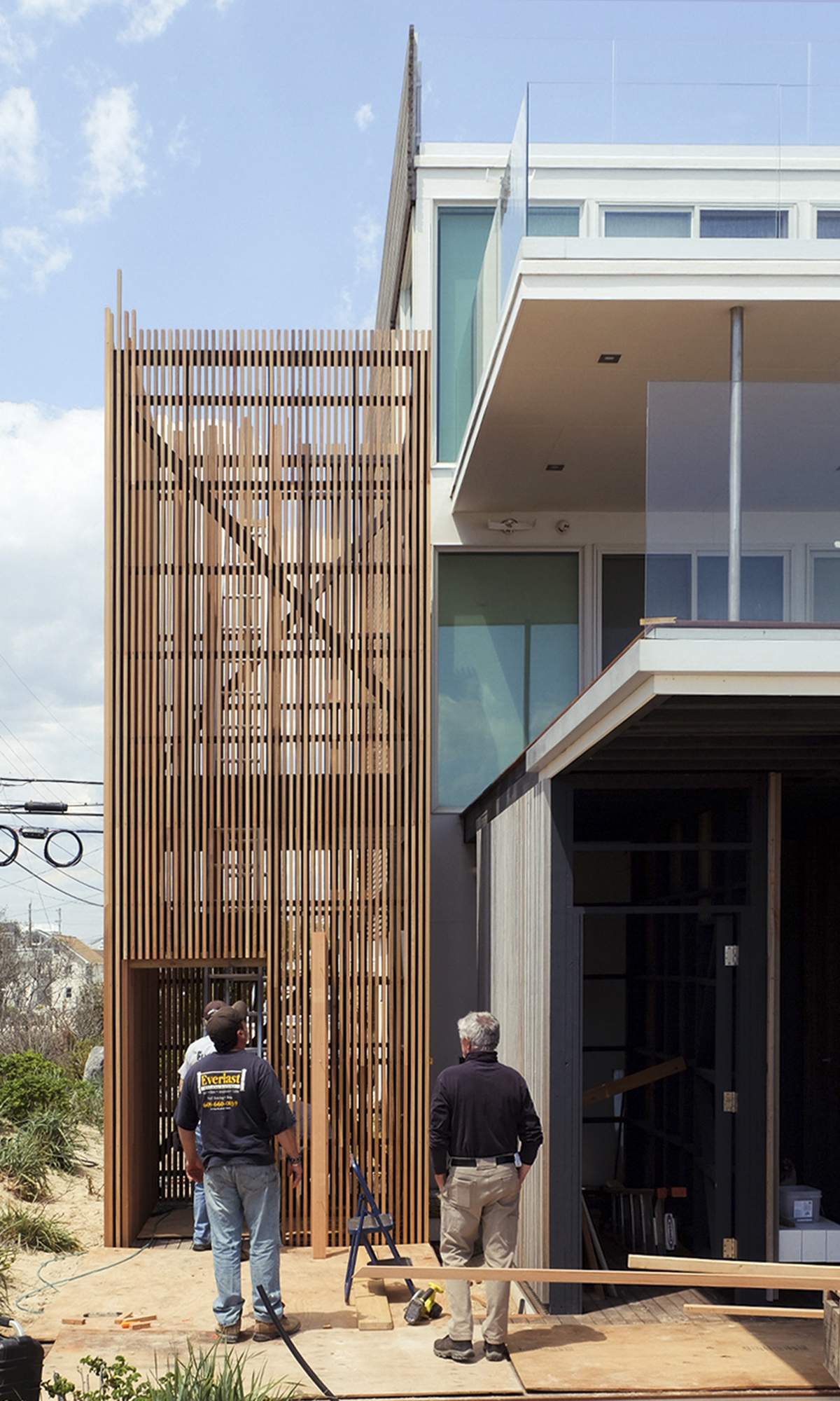 Construction photo showing the tall, vertical Red Cedar slatted screen box being installed to enclose the new exterior spiral staircase at the Water House project.