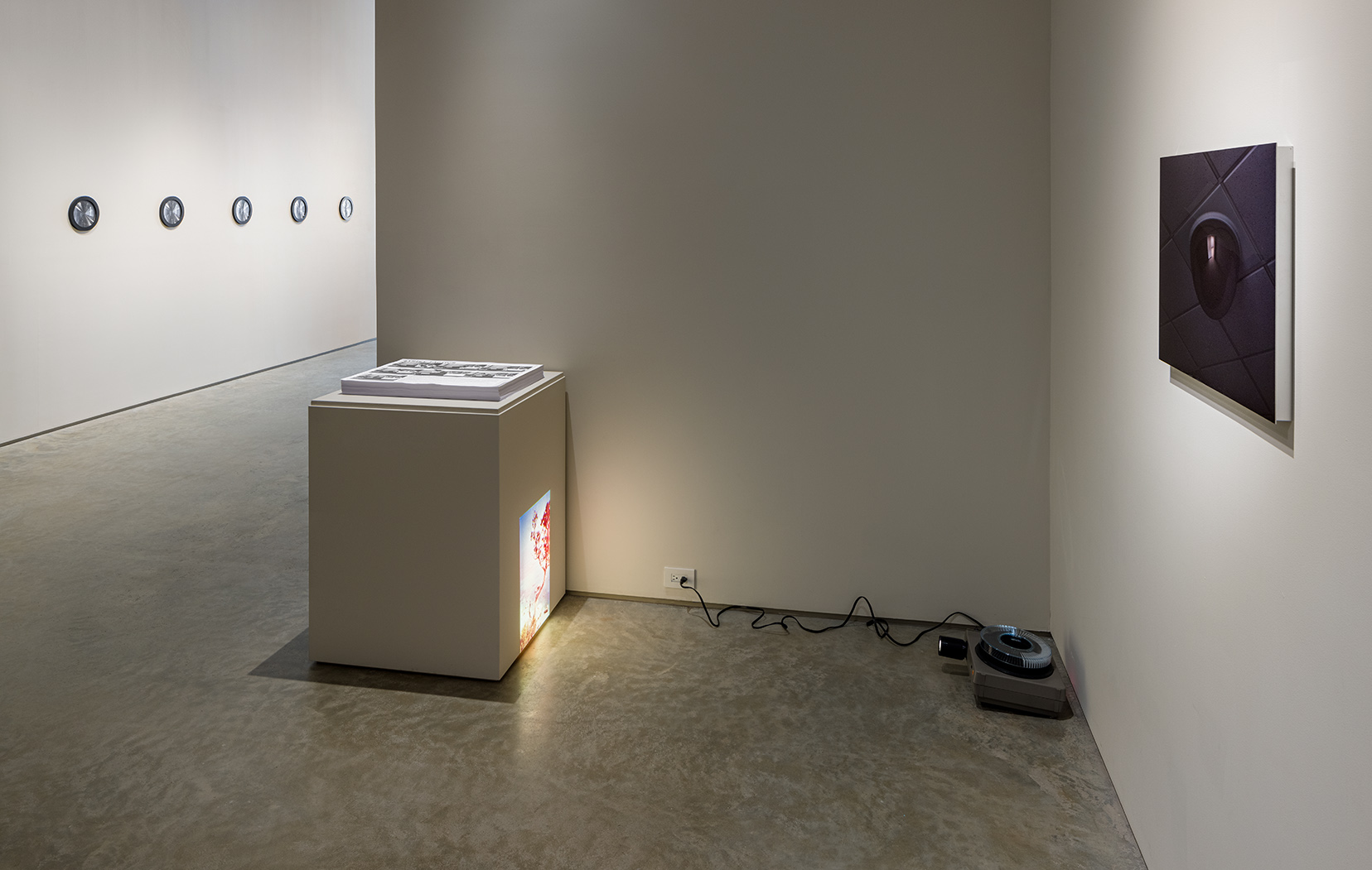 From left to right: Aura Satz, "She Recalibrates," 2018. Pencil on black paper, framed with lenticular magnifying sheet, diameter: 10 inches each; Jamal Cyrus, "Liberation Rotation (Ollie Towards a Metamorphosis)," 2020/2023. Stack of posters, 18 x 24 inches each; Jonathan Monk, "Today is Just a Copy of Yesterday (Holiday)," 2002. 40 color slides, slide projector, dimensions variable; Craig Kalpakjian, "Monitor," 1998. Cibachrome mounted on aluminum, 17 1/2 x 23 1/2 inches.Photo by Etienne Frossard.