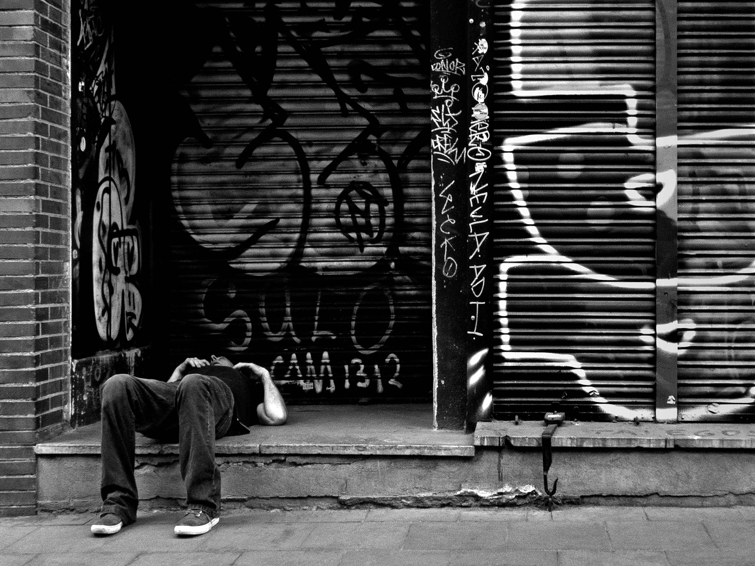 Man lying in front of a closed shop Barcelona, Spain, 2022photography, bw, single