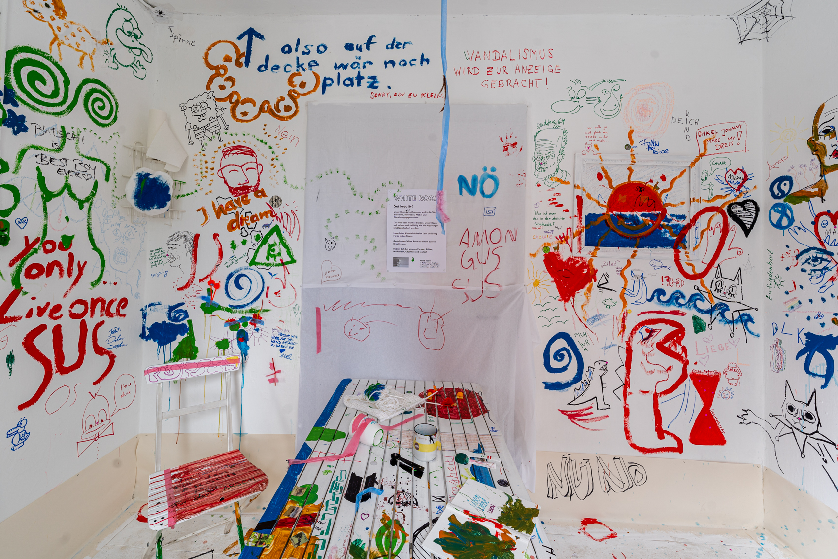 Bild 2 zu White Room:  In dem bunt bemalten Raum steht ein Tisch mittig. Auch dieser wurde bemalt.