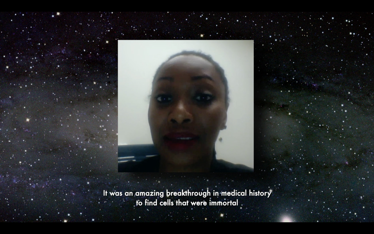 Dr Hadiyah-Nicole Green speaks to the camera. She is sitting in a white room. Behind her image is the Andromeda constellation.