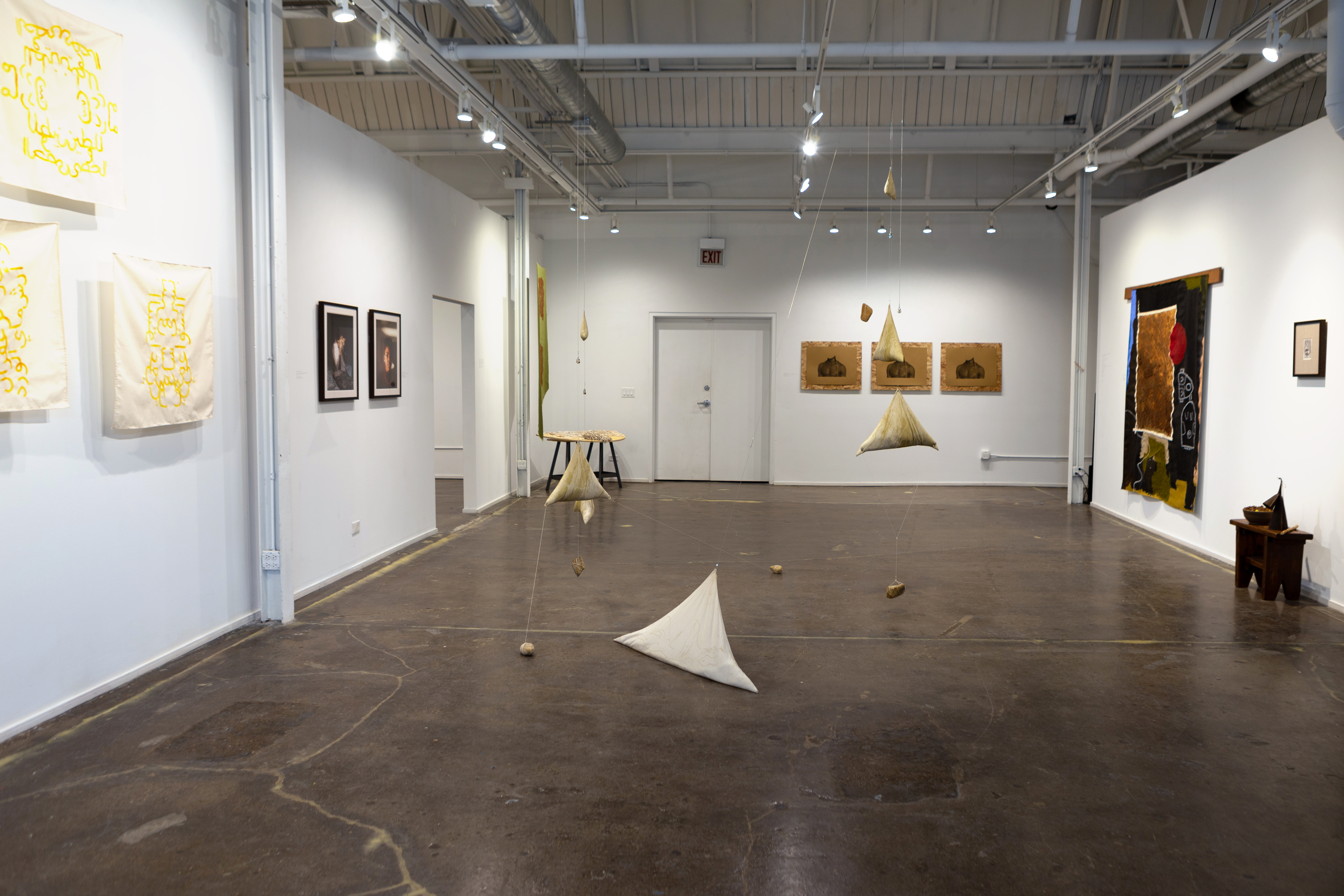 Wide view of an art gallery exhibition with objects on the white walls and on the gray concrete floors.
