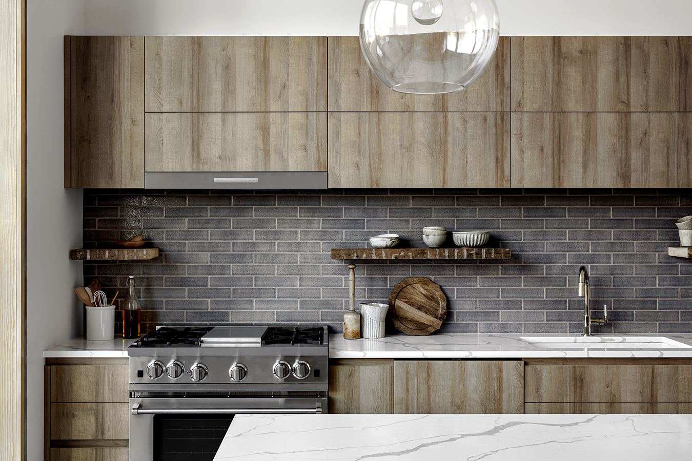 Kitchen with gray tile backsplash, white marble counters, and light wood cabinets