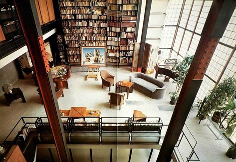 Maision de Verre’s great living room taken by the second floor. The room has a grand book case filled with books and gorgeous furniture. There is black and red industrial beams supporting the open concept.
