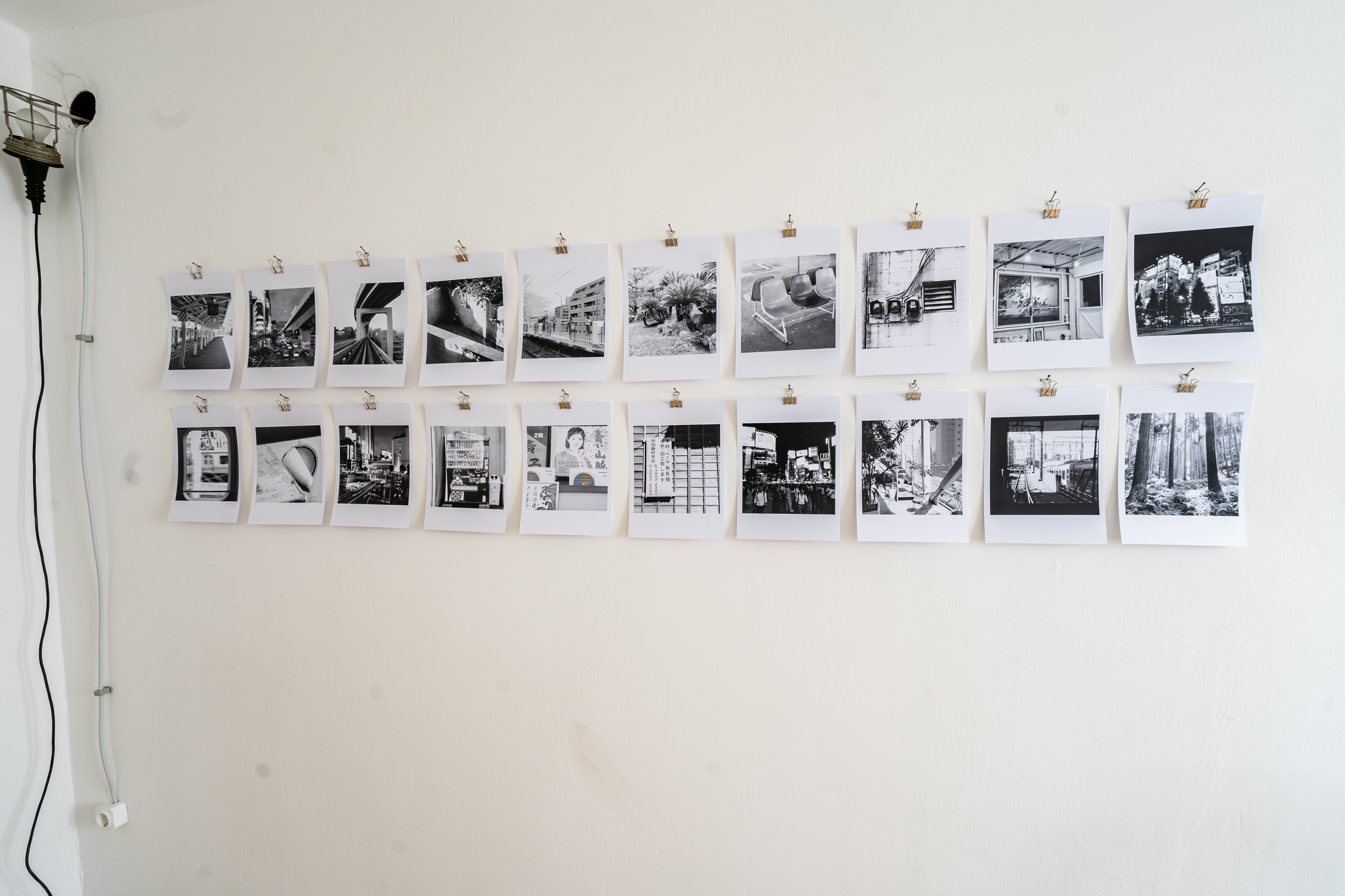 Bild 3  zu Neometropolis: Betritt man den Raum, h&auml;ngen an der linken Seite der Wand zwei Reihen mit je 10 quadratischen Schwarz-Wei&szlig;-Fotografien auf wei&szlig;em Din A4 Papier gedruckt. Die Motive zeigen vorwiegend &ouml;ffentliche R&auml;ume in St&auml;dten,  sowie die Fotografie eines Waldes.