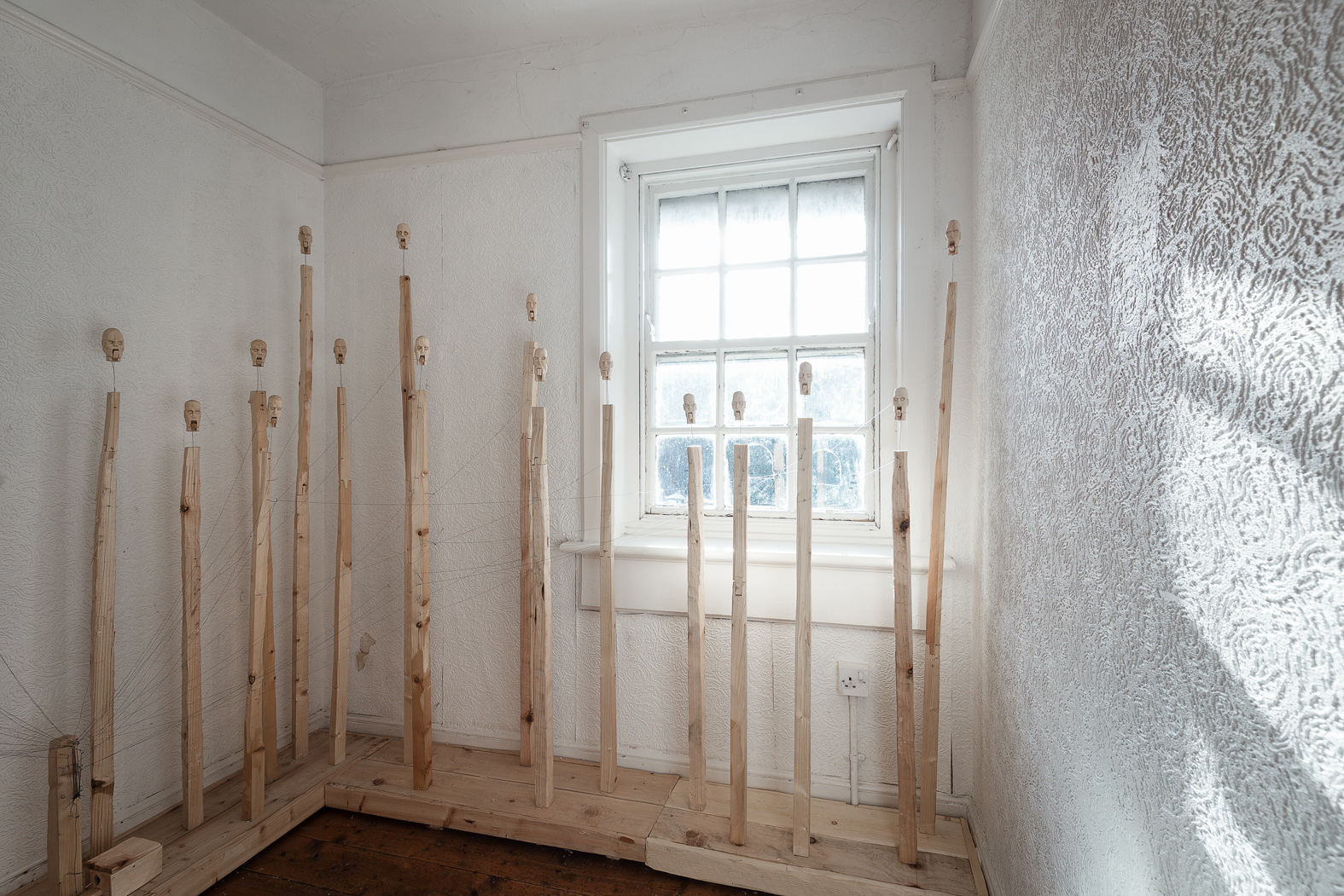 Galvanic Interruption 2017-2018. Kinetic sculpture consisting of 29 carved wooden heads. Materials: pine, found timber, thread, lace pins, electric motor, timer switch. Dimensions variable