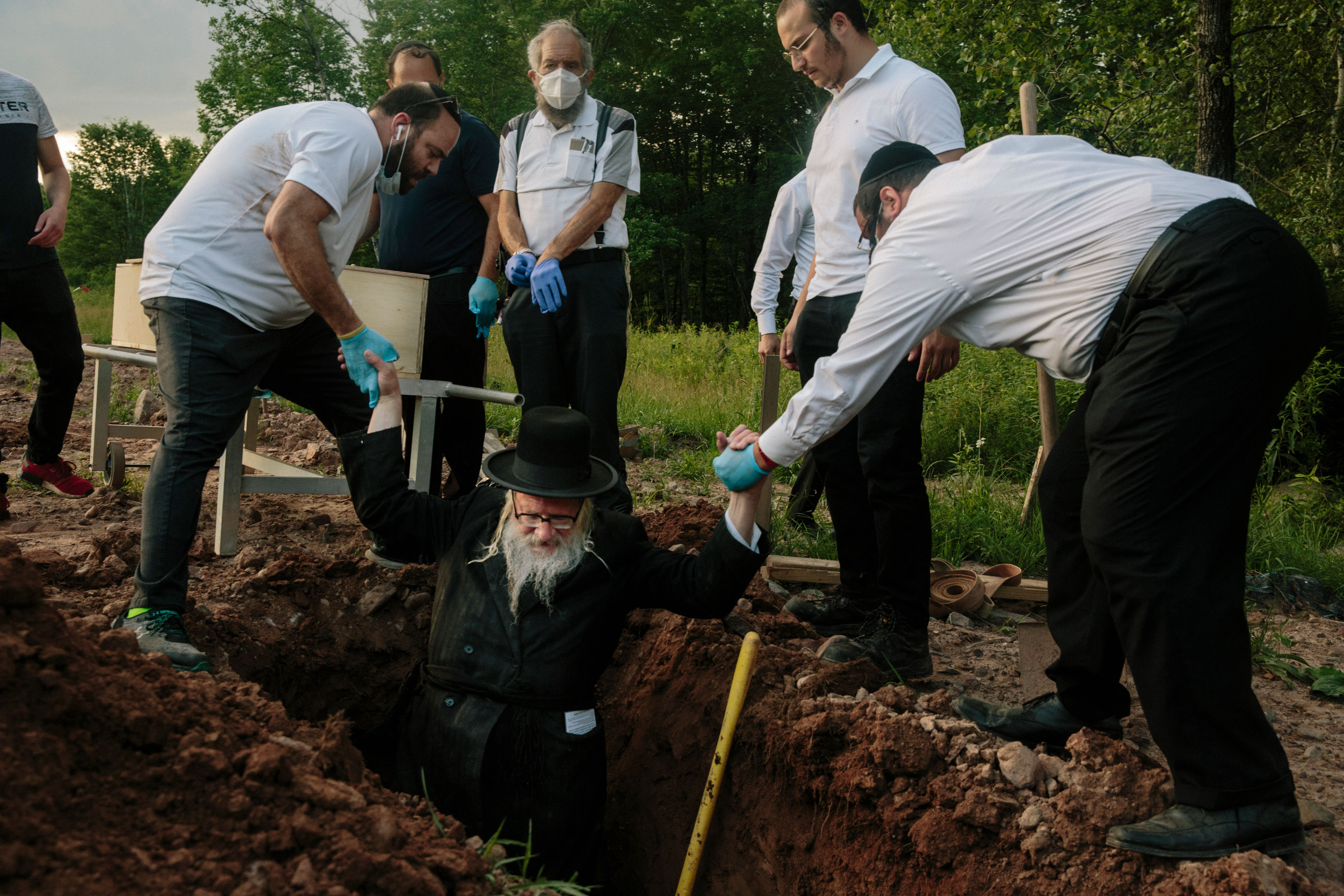 Rabbi Yakov Kellner is lowered into a grave by fellow volunteers to make adjustments. The deceased was a male COVID-19 victim who died a month prior in New York and was found unclaimed in a temporary refrigerated truck morgue.