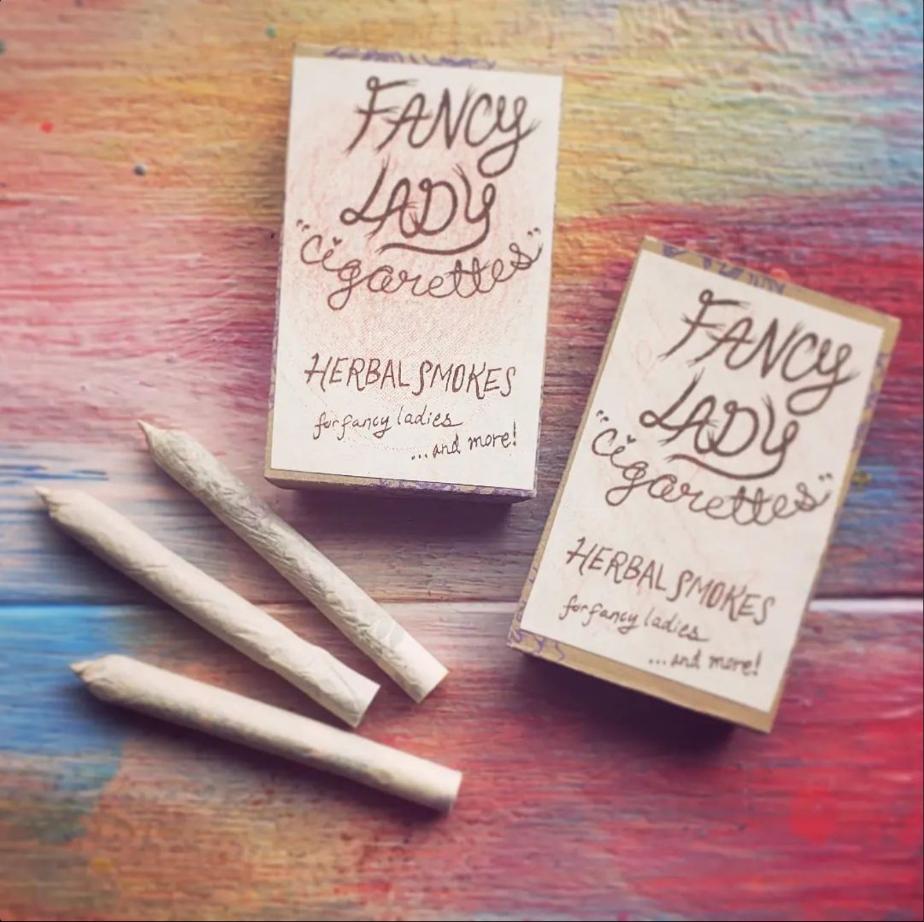 Two packs of Fancy Lady Cigarettes & 3 loose cigarettes on top of colorful painted wood