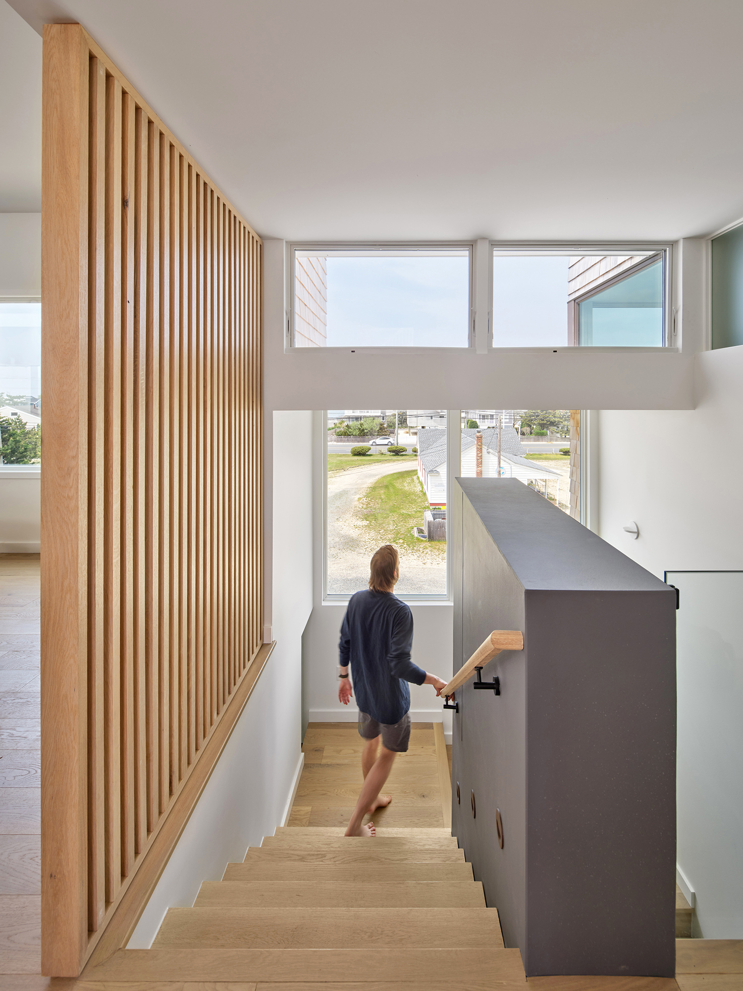 Architectural render of the Gap House main stairwell, featuring a floor-to-ceiling wood slat screen and a view to the street outside, highlighting the vertical flow of the interior.