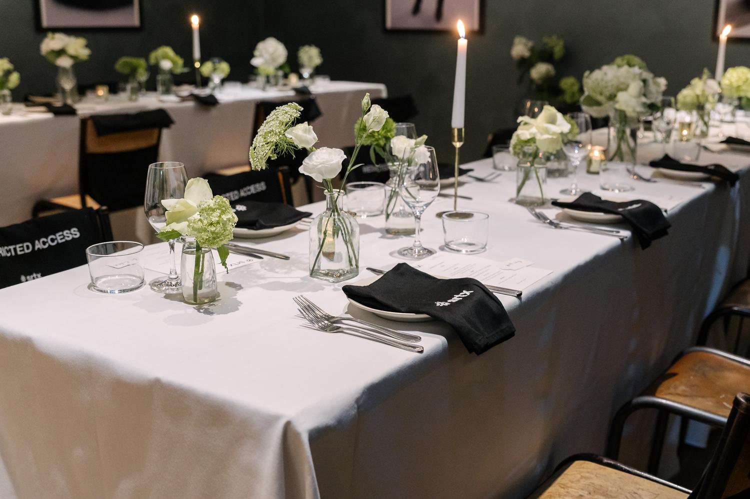 Elegant Sheertex brand activation dinner setup with white tablecloths, black napkins, candles, and floral arrangements.