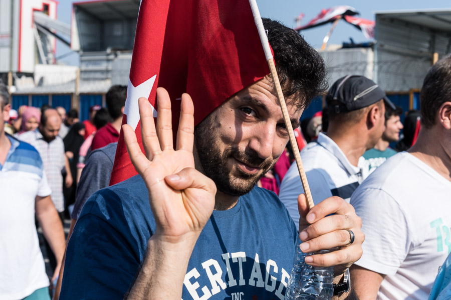 Yenikapi. Meeting pour la d&eacute;mocratie et les martyrs. Le symbole rabi'a que fait cet homme avec ses doigts &eacute;tait utilis&eacute; par les partisans de Mohammed Morsi lors du coup d'&eacute;tat militaire en 2013. Les partisans de l'akp l'ont adopt&eacute; par similarit&eacute;. Deux semaines apr&egrave;s le coup d'&eacute;tat avort&eacute; en Turquie, Erdogan organise un meeting g&eacute;ant sur la place de Yenikapi. Des millions de personnes d&eacute;ferlent dans les rues du quartier, la place et les art&egrave;res sont submerg&eacute;es par une mar&eacute;e humaine. Lors de ce discours, Erdogan annoncera l'orientation politique de son r&eacute;gime.