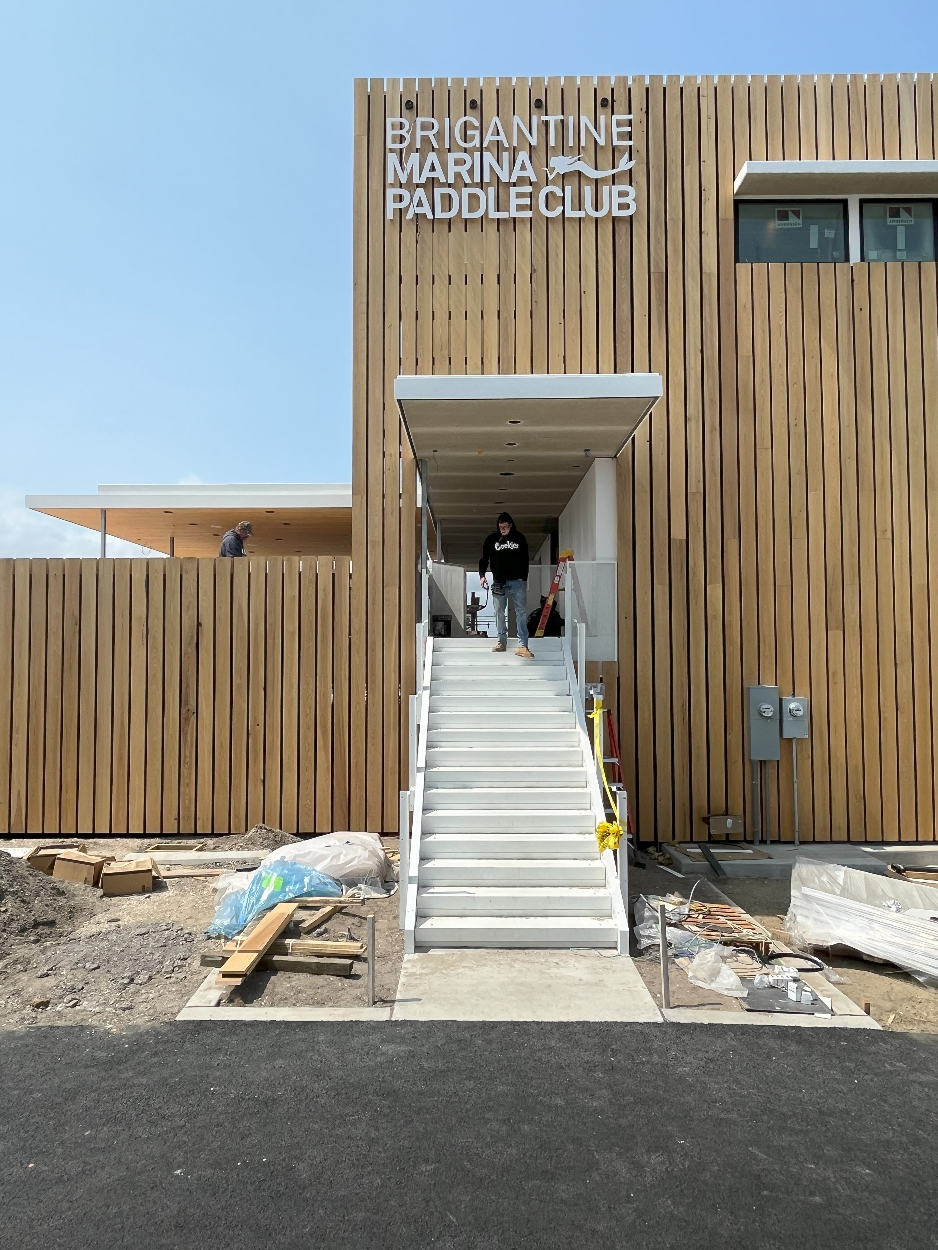 Construction photo showing the Brigantine Marina Paddle Club's main entry staircase and newly installed vertical wood cladding with prominent signage.