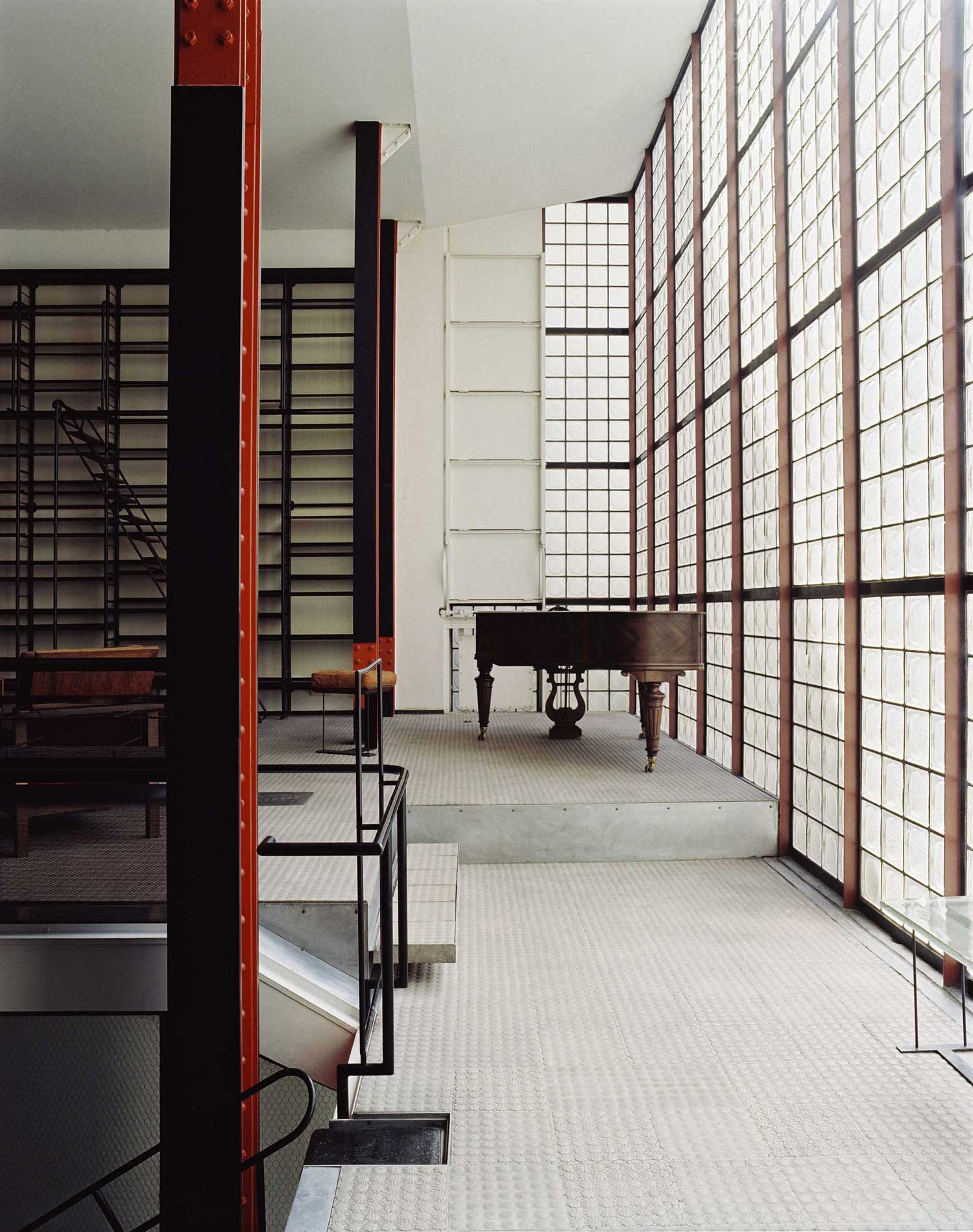 Another view of Maison de Verre’s great room featuring the glass brick wall and a brown grand piano.
