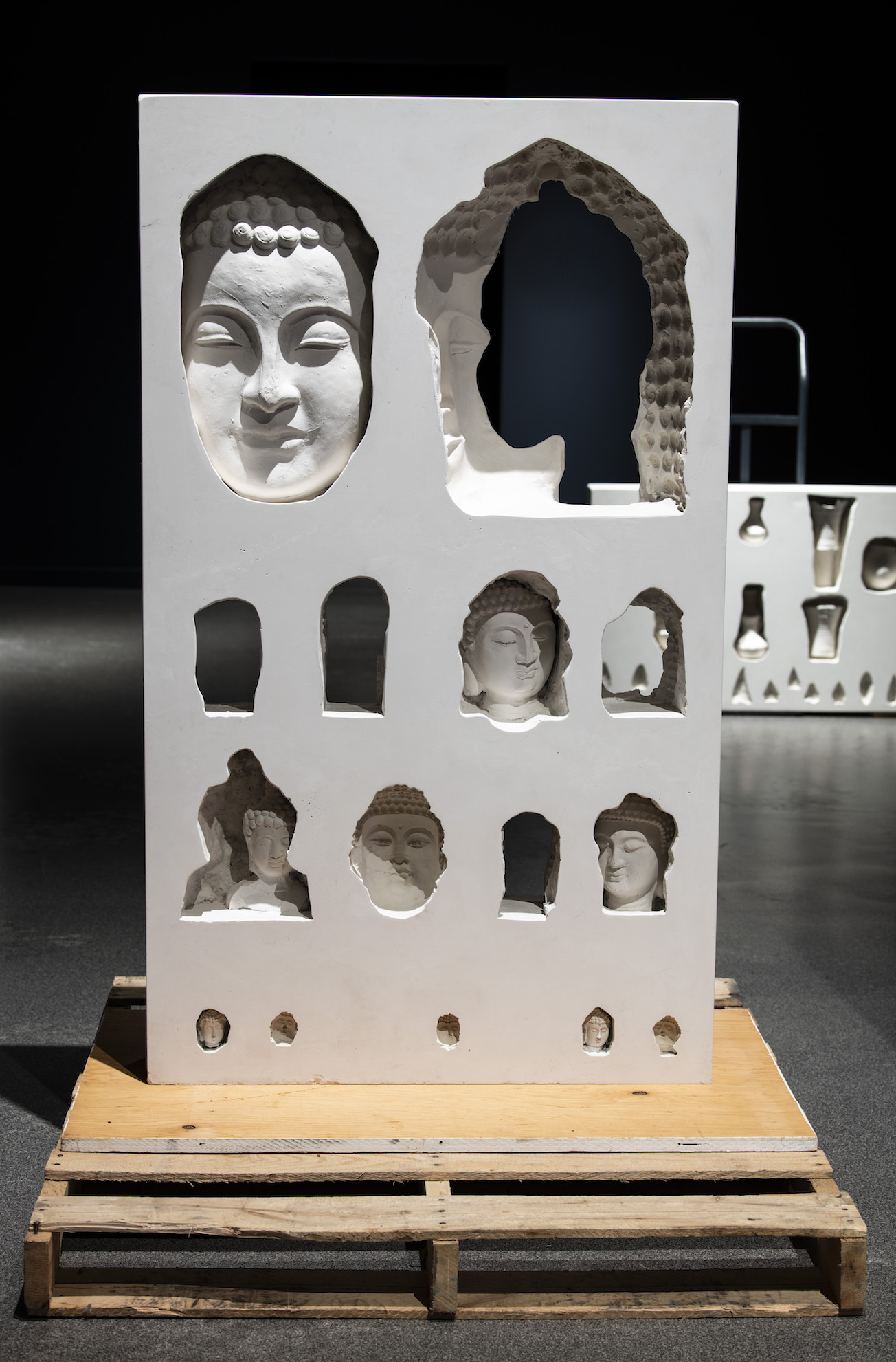 Foreground: Restitution Series (Buddha Heads), 2021, plaster, fibreglass, burlap, wood