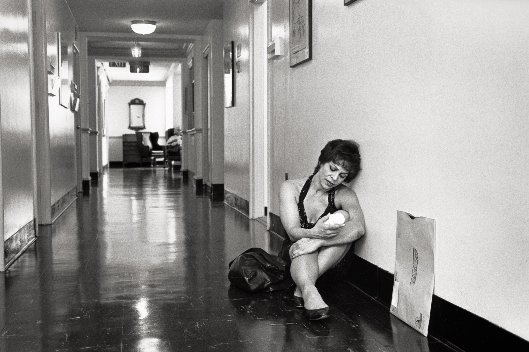 Diane waits outside her oncologist's office with her charts and bottle of liquid containing barium, awaiting a CT scan. A negative result provides momentary relief, but the continuous testing underscores the expectation that someday, somewhwere, the cancer may return.