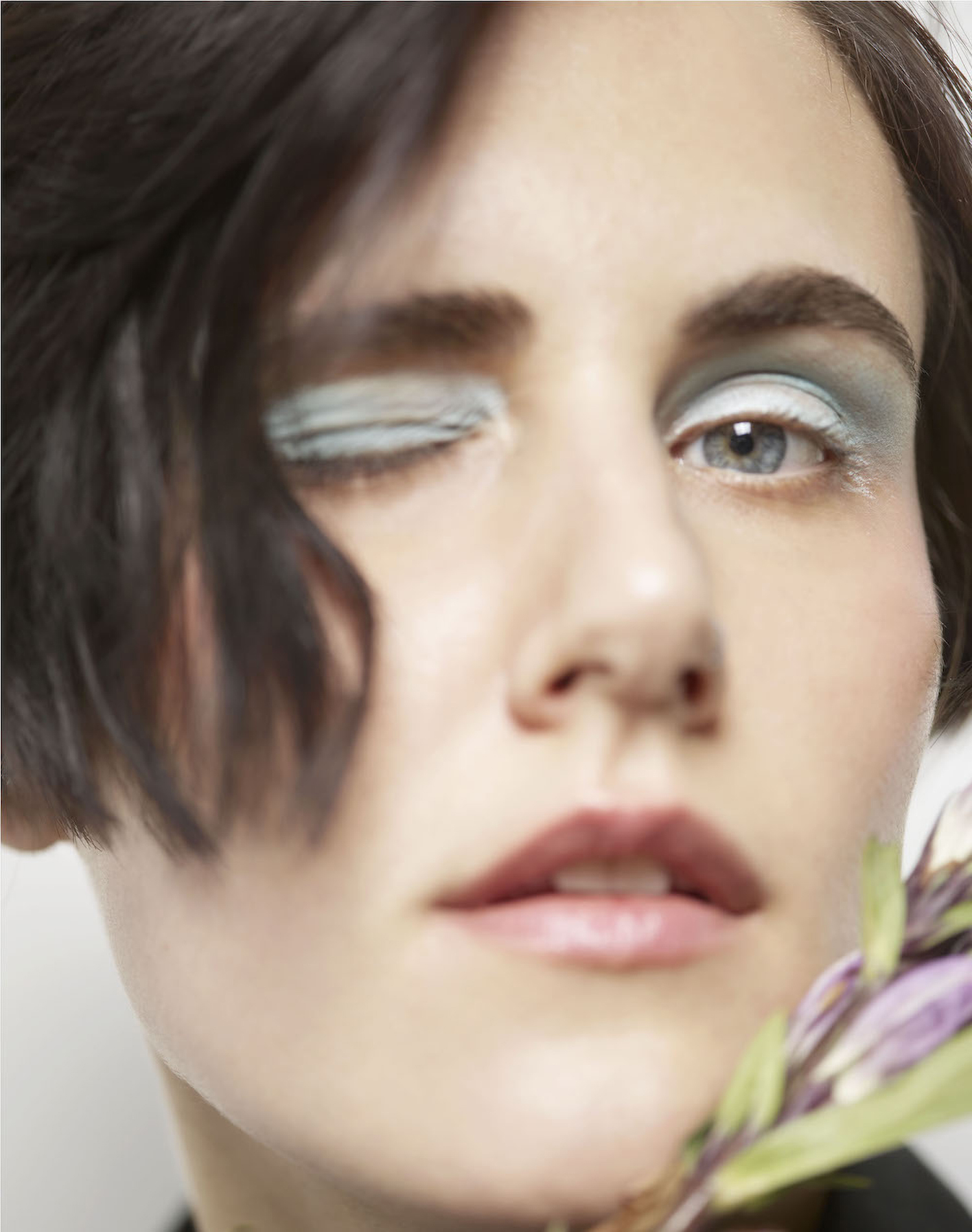 KMA photographer Daniel Schweizer shoots a closeup of a dark haired woman with blue eyeshadow holding a pink flower