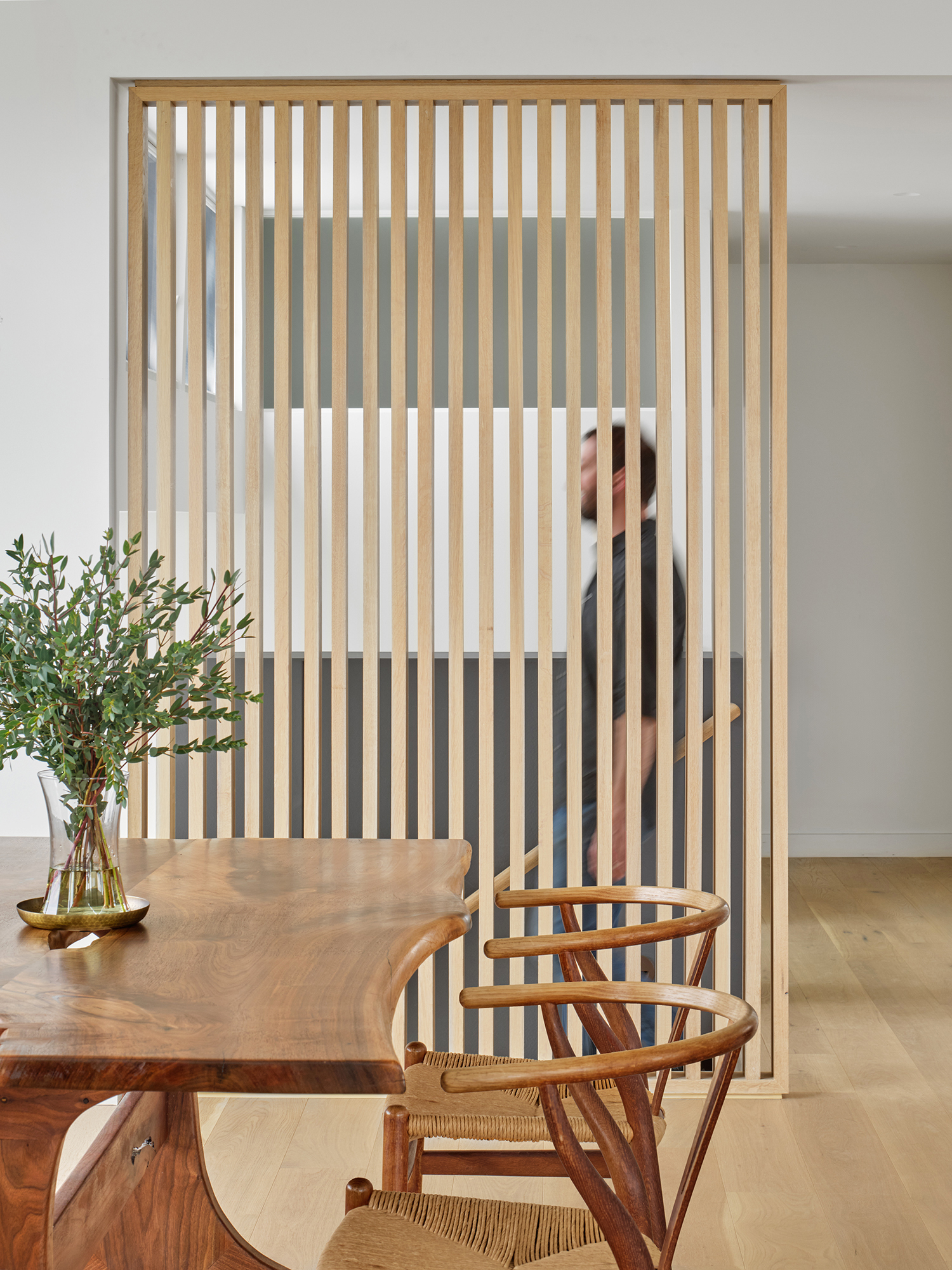 Interior render of the Gap House showcasing a modern wood slat screen wall that acts as a visual and physical divider, subtly separating the dining area from the adjacent staircase and vertical circulation.