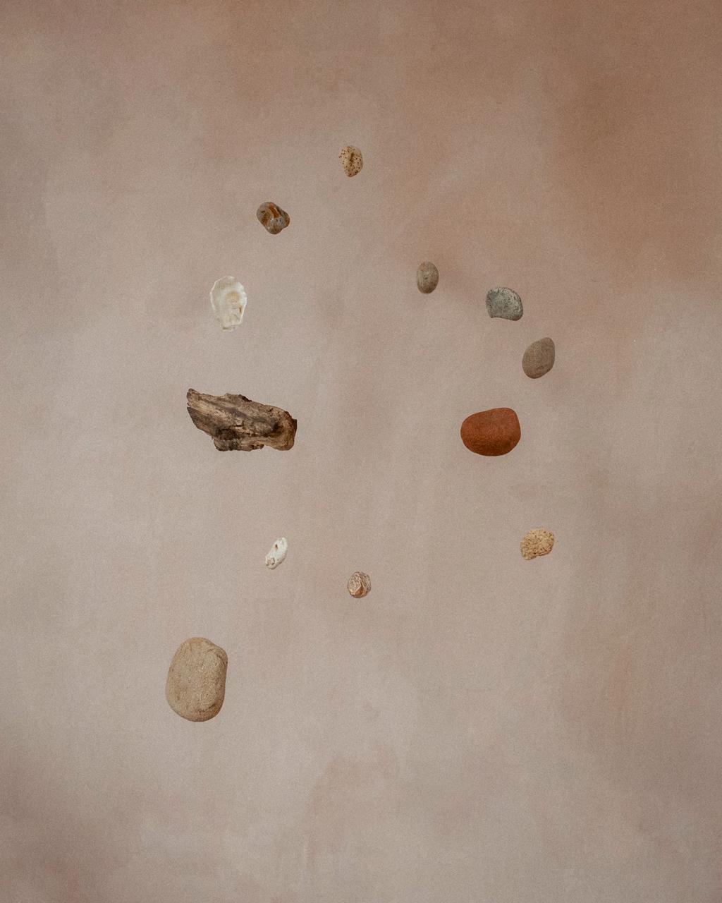 Planet in a Pebble by Seungwon Jung.  This series of photographs captures a mobile sculpture made of natural found objects such as pebbles, shells and driftwood. Wave smoothed pieces of rock, remnants of shells that once offered shelter for marine life, spin, turn and revolve around one another like small planets, forming their own solar system. By putting different natural forms together and balancing them on a mobile, I wanted to show the interconnectedness of the many entities that co-exist on this planet, highlighting the often-invisible care that we give to, and receive from one another.