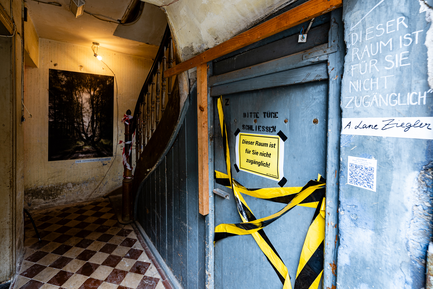 Bild 1 zu Dieser Raum ist f&uuml;r Sie nicht zug&auml;nglich: Blick in das alte Treppenhaus vom Haus  Reality 2 mit braun-wei&szlig;en Fliesen. Gleich rechts neben dem Eingang unterhalb der Treppe befindet sich eine blaue T&uuml;r. Diese ist mit gelb-schwarzem Absperrband und einem gelben Schild versperrt, auf dem in schwarzer Computerschrift "Dieser Raum ist f&uuml;r Sie nicht zug&auml;nglich" geschrieben steht.