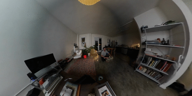 gif of an wide image zooming through the living room of a person while they are in the background playing the bongos.