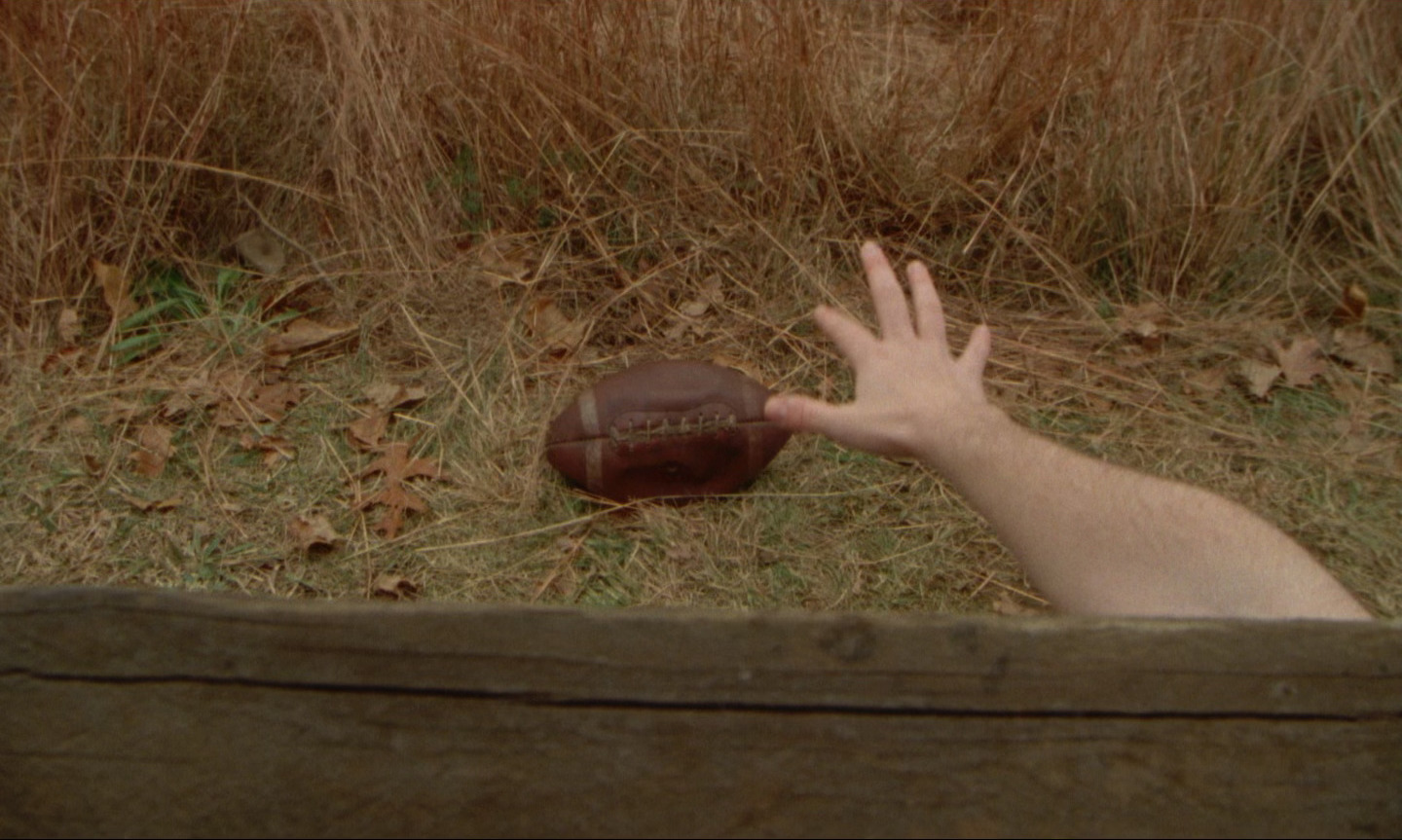 still image from film showing hand reaching for football