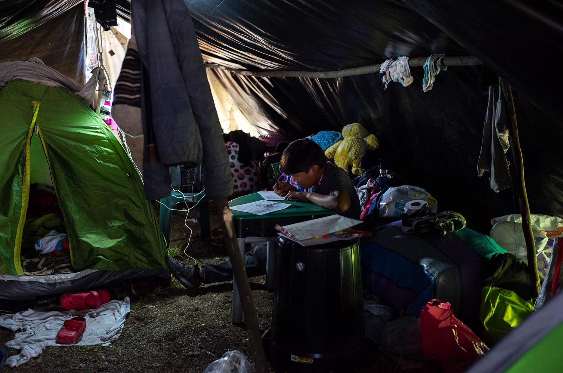 A young boy does his homework in the hut designed for his family. The various communities have tried to ensure that their children have access to school education. Volunteers from outside the government filled the role of teachers.