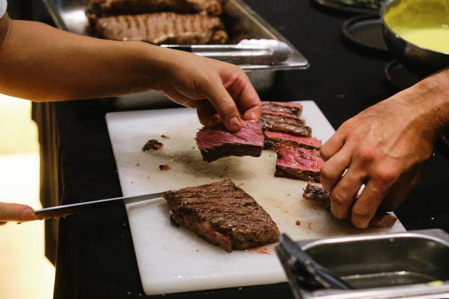 Chef slicing medium-rare steak on a chopping board during a Paired London dinner, close-up of hands plating meat.
