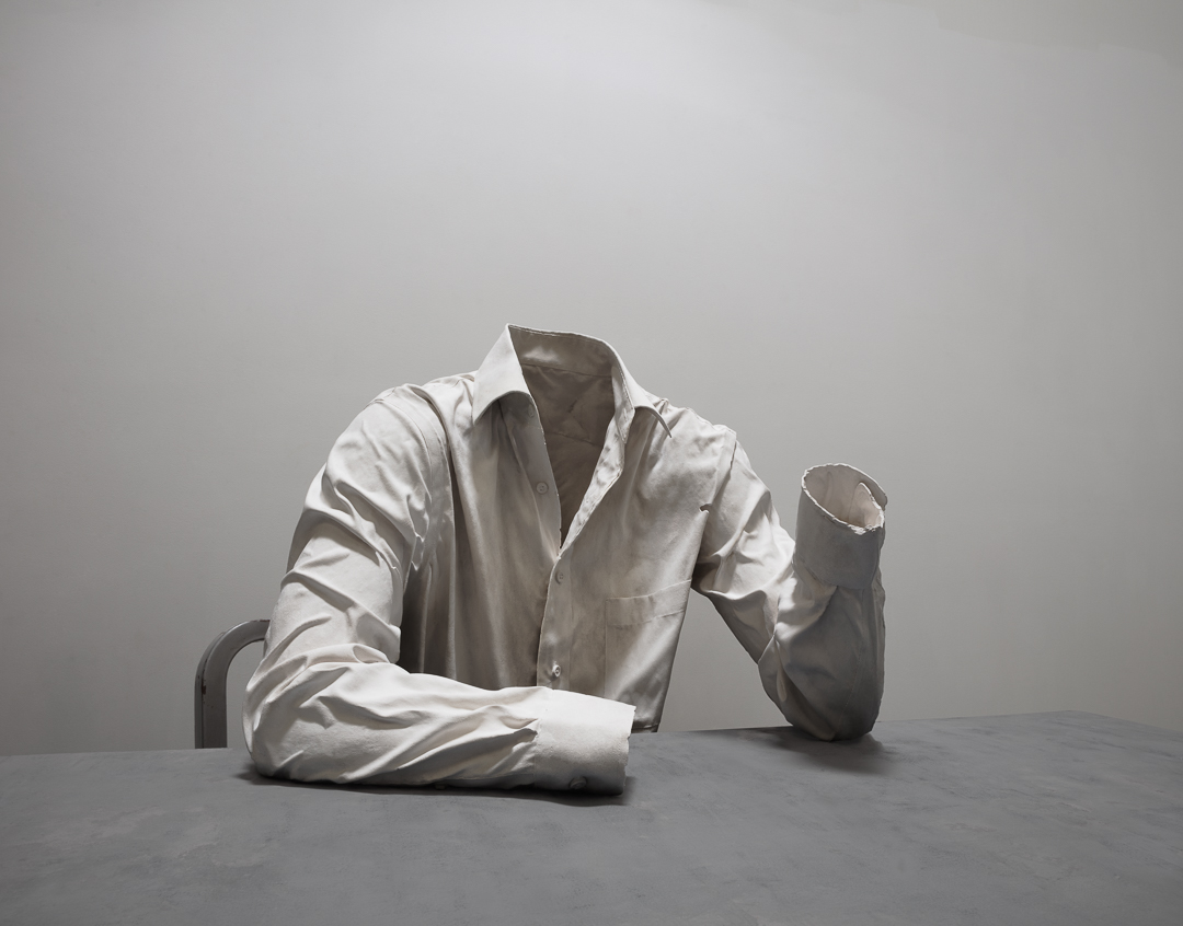 a men's button up shirt cast out of plaster sitting at a desk, there is no figure in the shirt