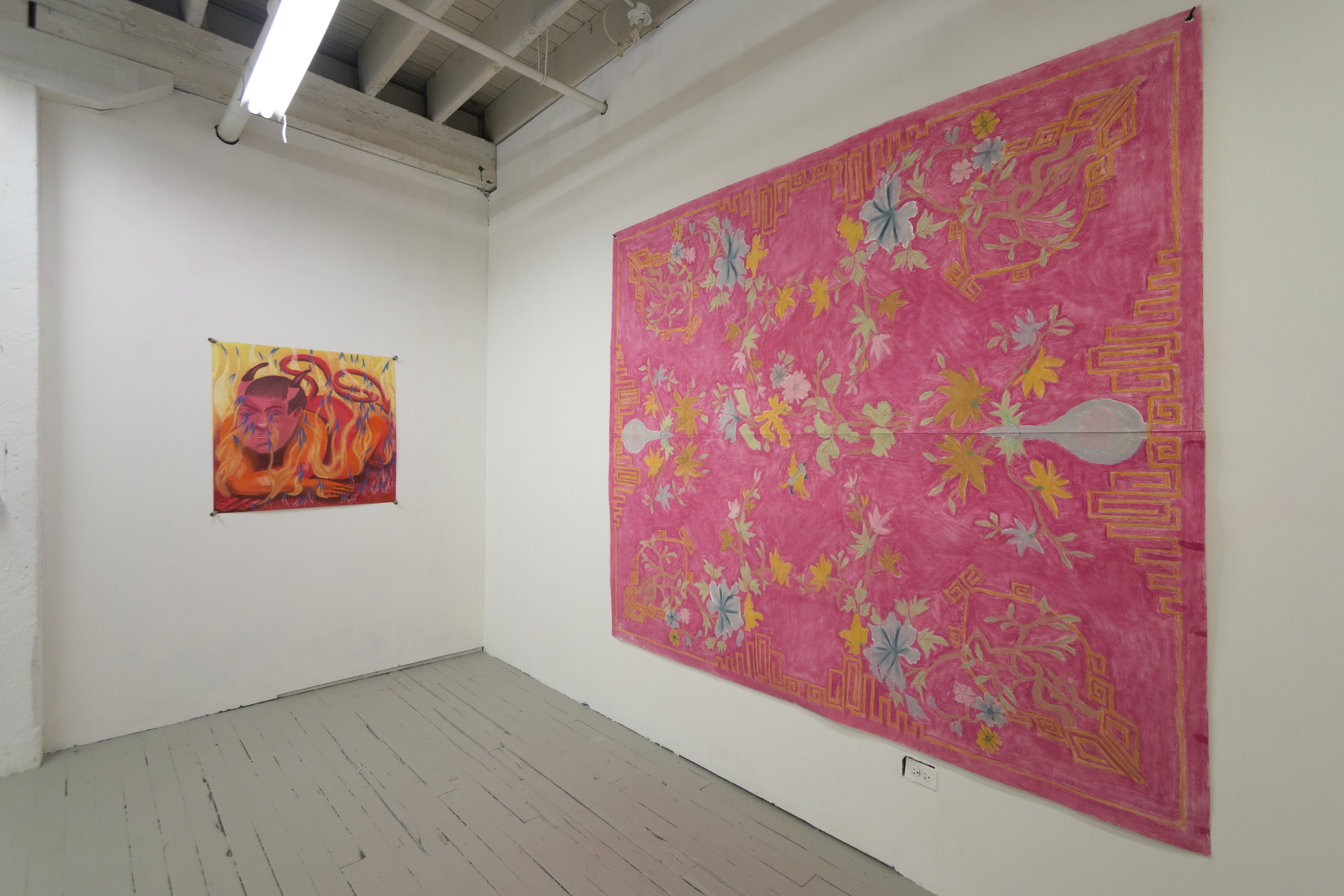 An installation shot of the exhibition Amor de mis Amores. In focus is a large drawing that is mostly in shades of pink, with yellow and blue flowers, and mimics a large tapestry. On the left wall beside it is a small drawing of an orange figure with horns on their head, surrounded by flames.