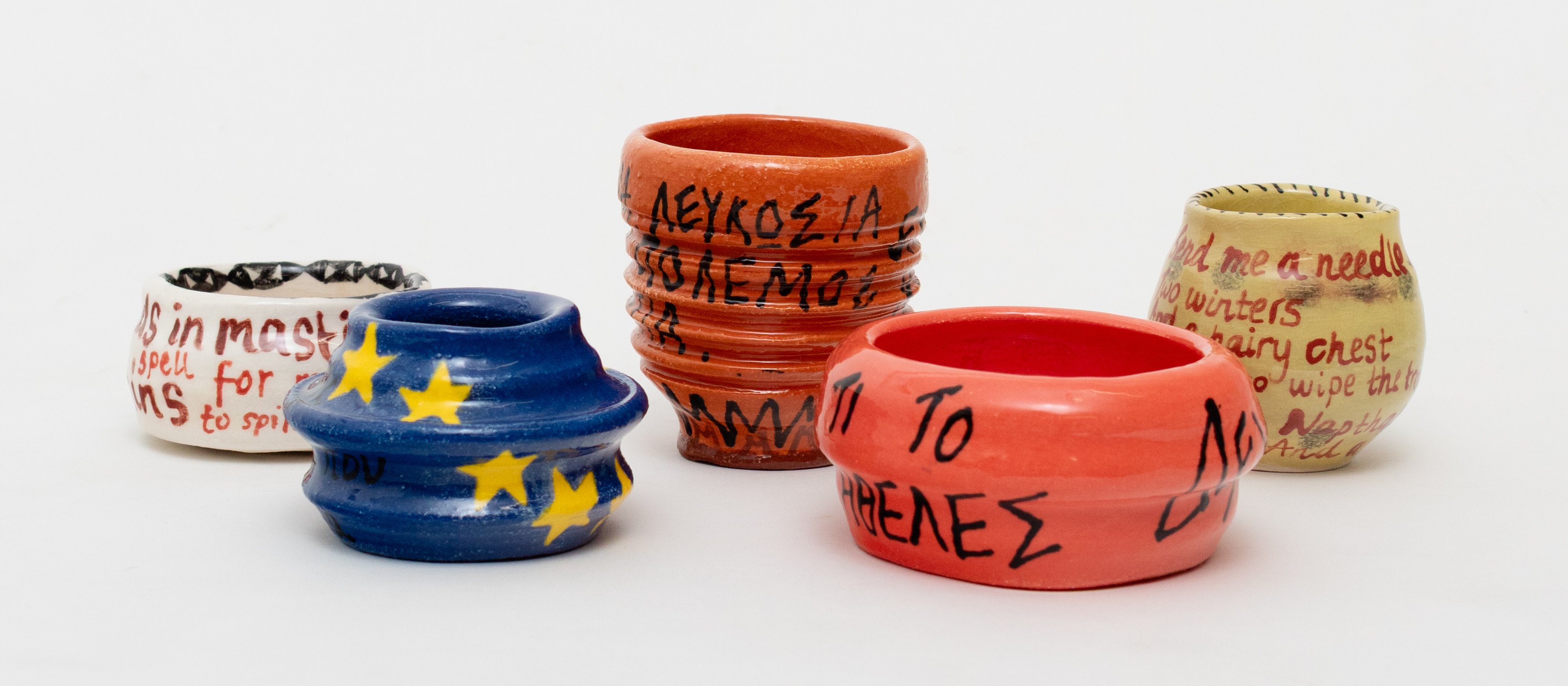 From left to right: Constantina Iacovou, Spell work, 2025, Ceramic vessel, 5 x 10 cm; Constantina Iacovou, You who loves the sea, bathe poorly, 2025, Ceramic vessel, 6.5 x 10 cm; Constantina Iacovou, Αykupα, Aθήvα, Λευκωσία - Εχθρός μας είναι ο πόλεμος και η στρατοκρατία [Ankara, Athens, Lefkosia - Our (common) enemy is war and militarisation], 2025, Ceramic vessel, 10 x 9 cm; Constantina Iacovou, ΔEXTHKA, ΔΈXTHKEΣ. TI TO HΘEΛEΣ;  [I agreed, you agreed. What did you want it for?], 2025, Ceramic vessel, 6 x 12 cm; Constantina Iacovou, Dear Santa, 2025, Ceramic vessel, 8 x 8.5 cm