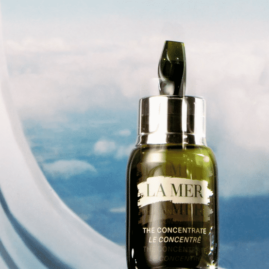KMA photographer Vincent Gapaillard shoots La Mer Concentrate bottle in front of airplane window with blue sky and clouds in view
