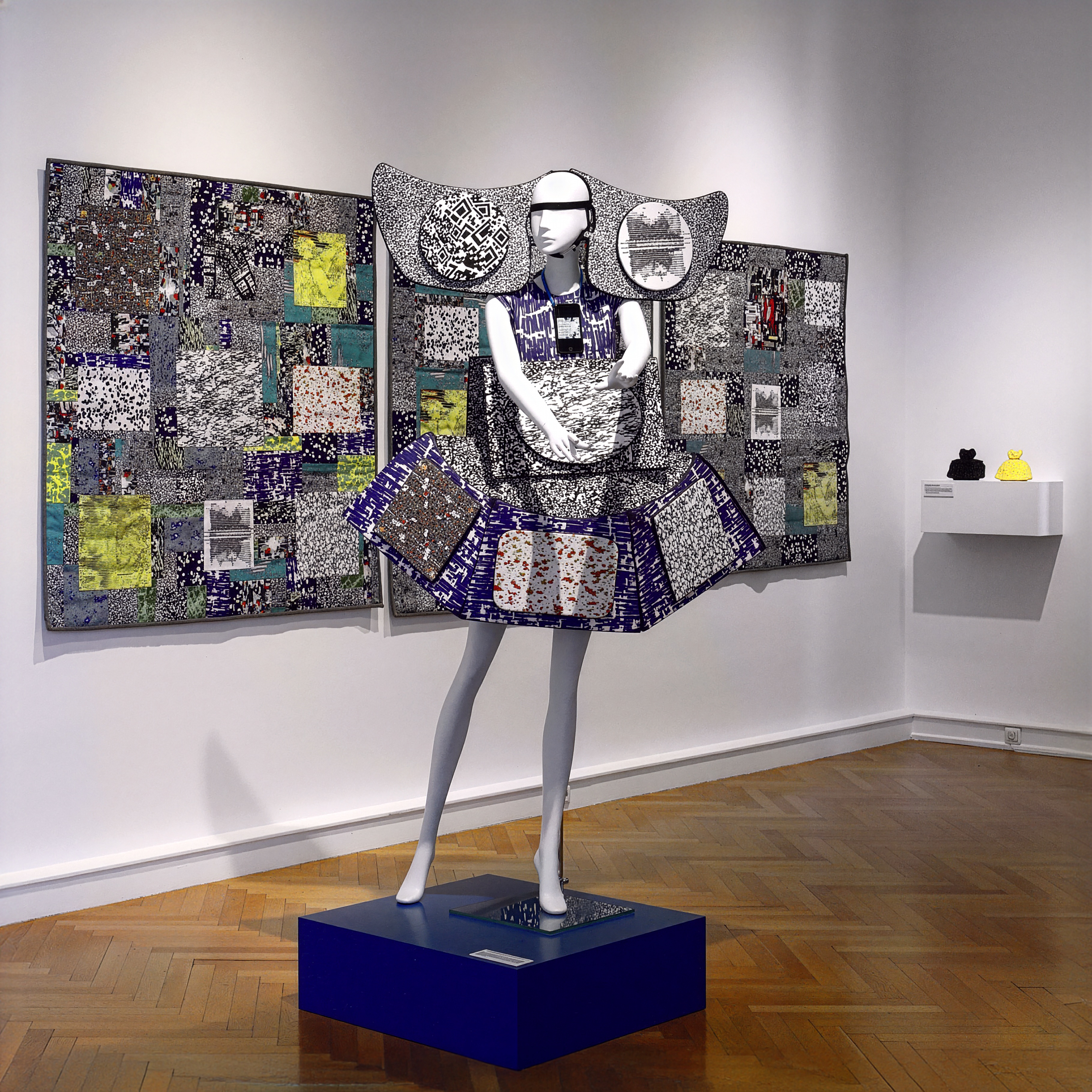 Julie Website Dresses (2013-2014), augmented trackable custom fabric, using dye sublimation  computer-printed on polyester canvas, mounted on EVA foam, and-sewn and glued, implementing  the web-based Alices App, triggered by QR to display text animations of the Alice’s Walking libretto;  Blue Ascii Girls Quilt, Big Crazy Quilt; Nayland Split Square Quilt (all 2014),   also made from augmented trackable custom fabric using dye sublimation computer-printed  polyester canvas, mounted on EVA foam, hand-quilted by using a mechanical plastic labeling tool,  also implementing web-based Alices App triggered by QR.
