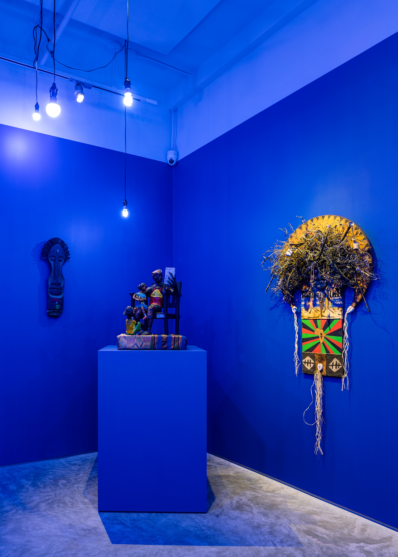 From left to right: "Hair Hard As Nails," 1998, wood, old nails, paint, cowrie shell, beads.  "Each One Teach Two," 1995, papier-mâché, fabric, wood chair. Second metal sun is titled My Roots R. N. Afrika, 1998 Found scrap metal, raffia, paint, fabric, cowrie shells, Afro comb, 