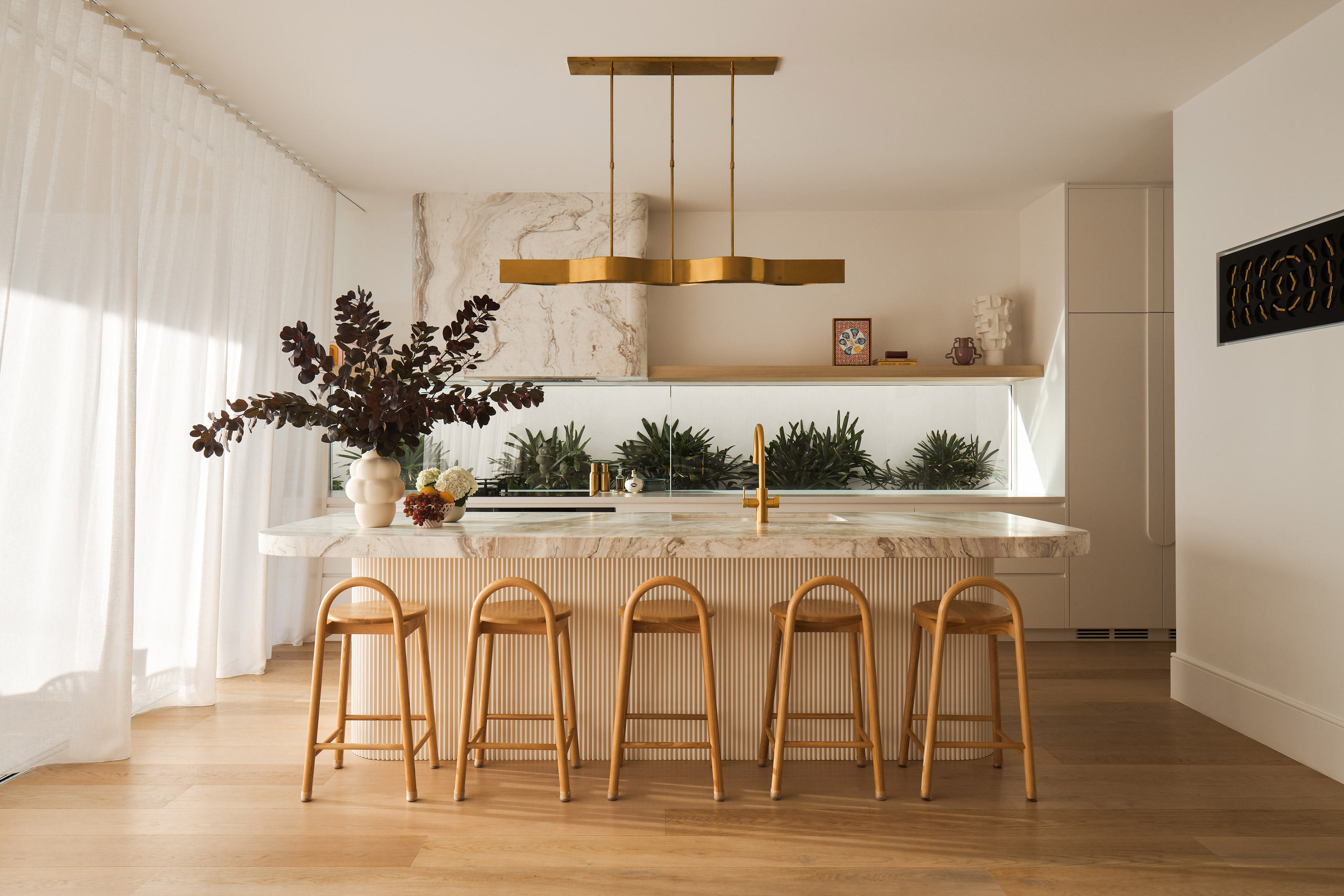 Luxurious light-filled kitchen space with stone benchtops and brass fixtures.