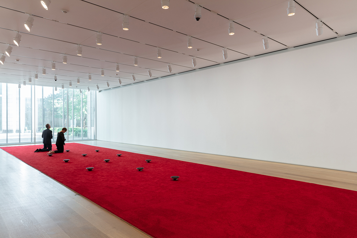 James Webb, Prayer (2000 - ongoing) | Carpet, speakers, audio, 1600 x 400 cm | Installation view, Art Institute of Chicago, Chicago | link to audio Prayer is an ongoing project, remade around the world since its first presentation in Webb’s home city of Cape Town in 2000. The work consists of recordings of prayer from individuals who belong to dozens of faiths and spiritual affinities in the host city. Listeners are invited to remove their shoes and walk the length of the carpet, composing their own arrangement of voices as they go, or to kneel or otherwise lower themselves next to a speaker to listen more closely to particular prayers. The spare though colorful installation has the austerity of a work of Minimal Art and the enveloping richness of a choral concert.